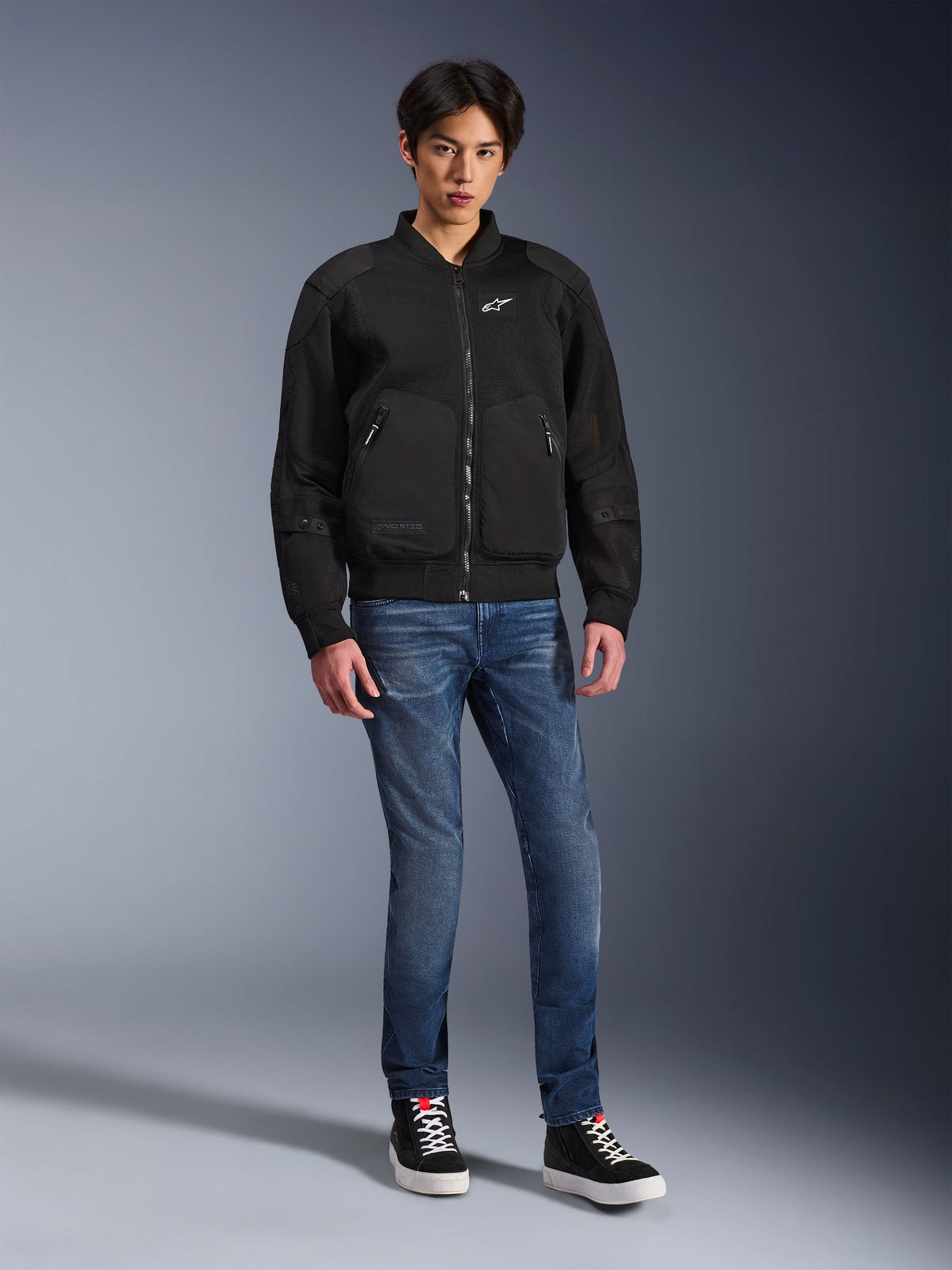 Alpinestars Flight Air Jacket, Black, urban-inspired bomber-style motorcycle jacket with 3D mesh panels and white chest logo, worn by a model with blue jeans and black sneakers, contemporary riding apparel