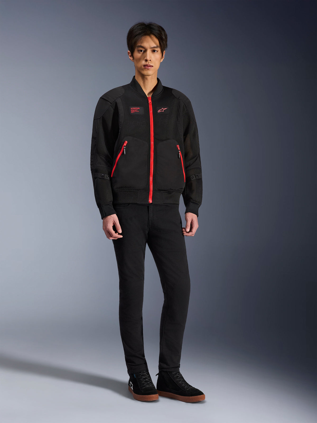 Alpinestars Flight Air-jakke i Black Bright Red, urban motorcykeljakke i bomber-stil med 3D mesh-paneler og markante røde lynlåse, båret af en model med sorte slim-fit bukser og sorte sneakers, street-inspireret moderne køreudstyr