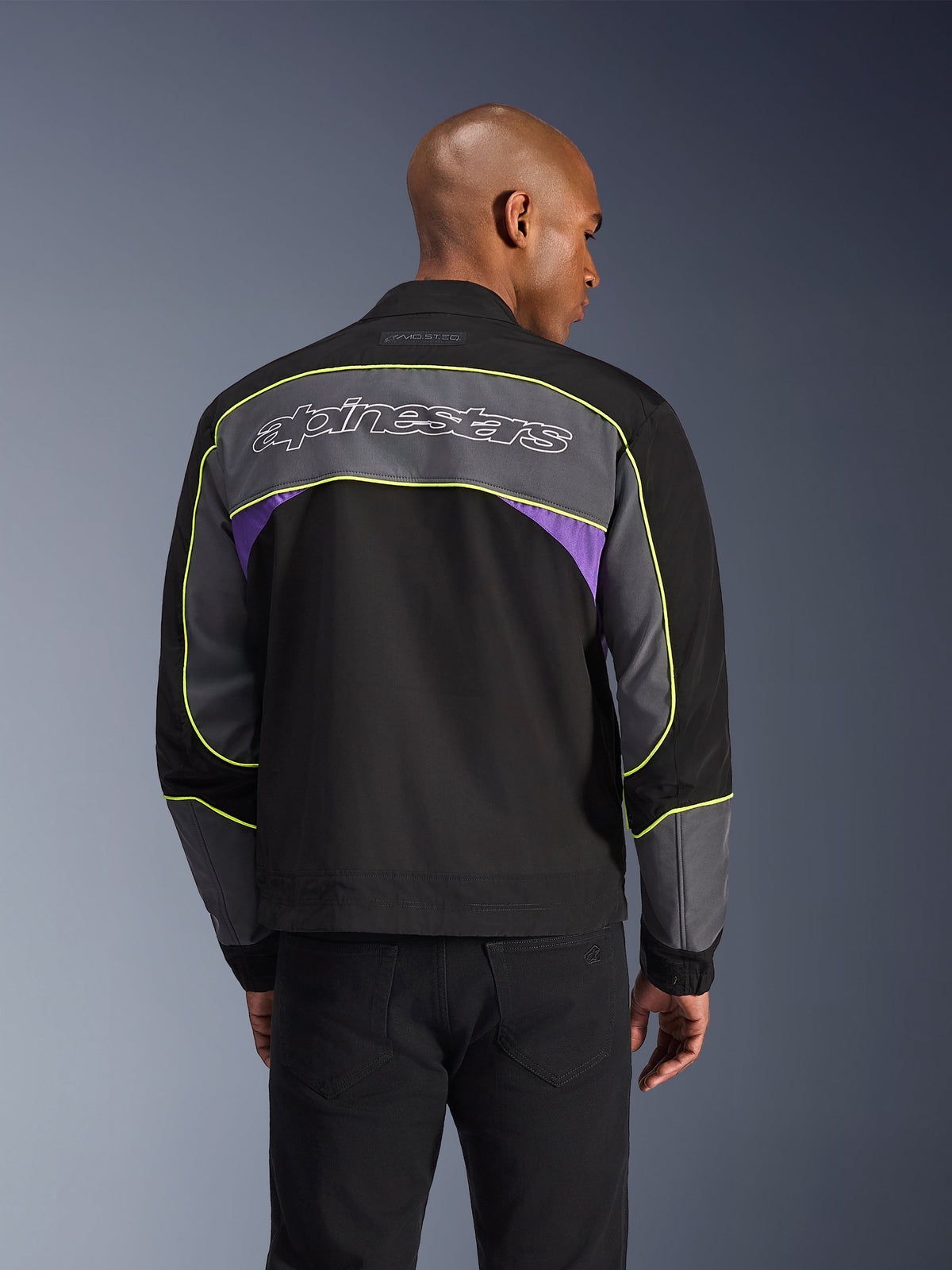 Alpinestars Unite jakke, urban motorcykeljakke, Black Asphalt Violet, set bagfra med grå paneler og violette detaljer, limegul piping, stort Alpinestars-logo på den øvre ryg, minimalistisk streetwear-design