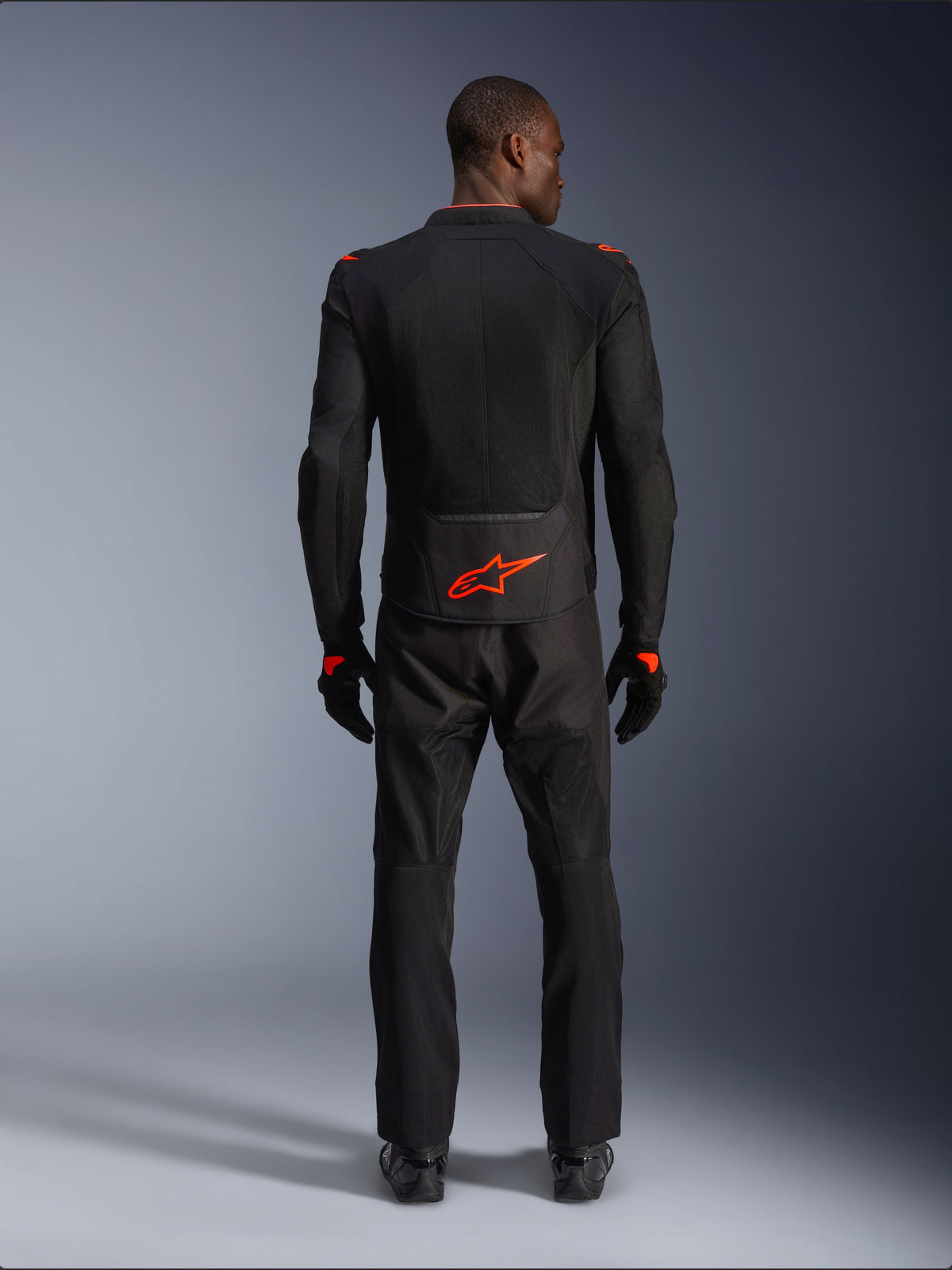 Alpinestars Viper Air V4 Jacket, Black and Red Fluo, rear view on model, worn with matching black riding pants and gloves, featuring a bright fluorescent red logo on the lower back, mesh construction for airflow, athletic fit for motorcycle road riding