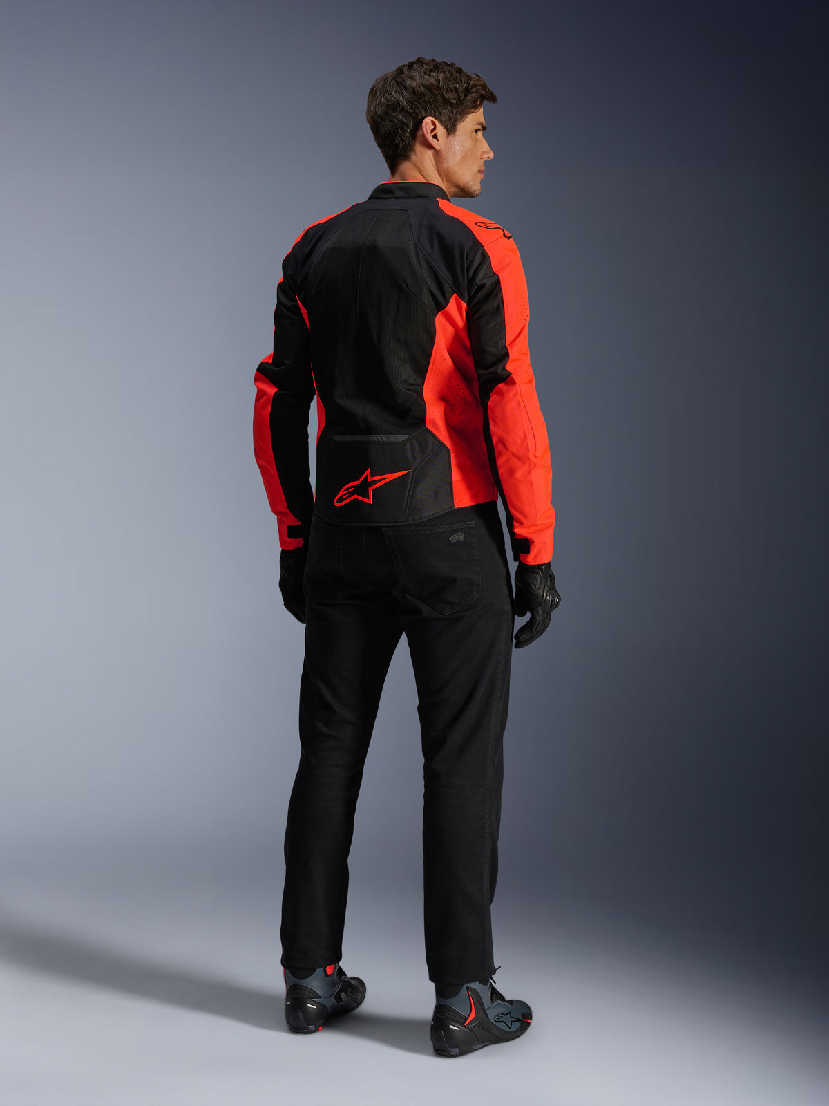 Alpinestars Viper Air V4 jakke, Red Fluo Black, set bagfra på model, med tekniske mesh-paneler og et rødt stjernelogo nederst på ryggen, kombineret med sorte motorcykelbukser og handsker for et komplet look til landevejskørsel.