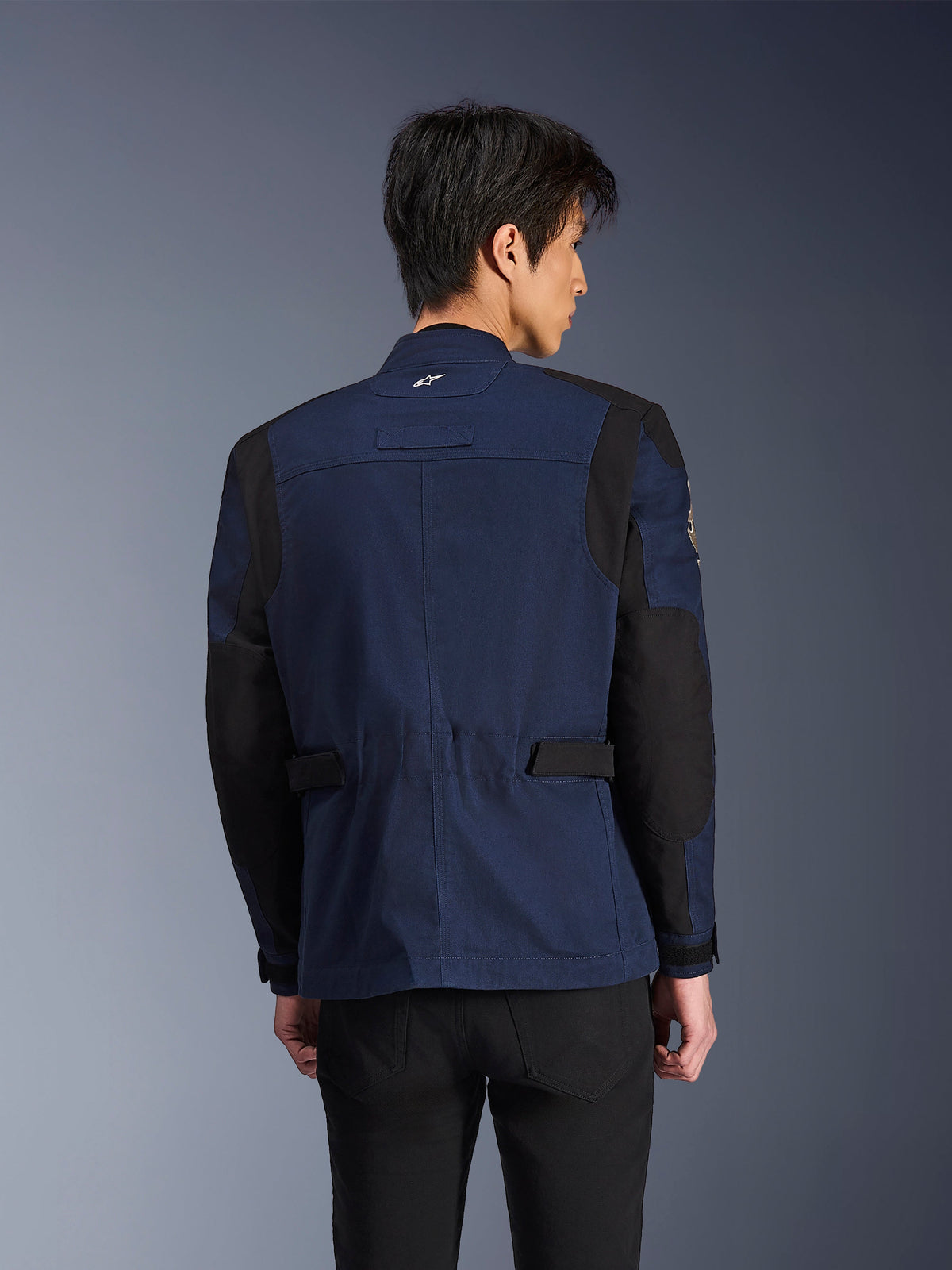 Alpinestars Dice Jacket, mørkeblå og sort urban field-motorcykeljakke, set bagfra båret af en mand, med forstærkede sorte skulder- og albuepaneler og justerbare stropper i taljen.