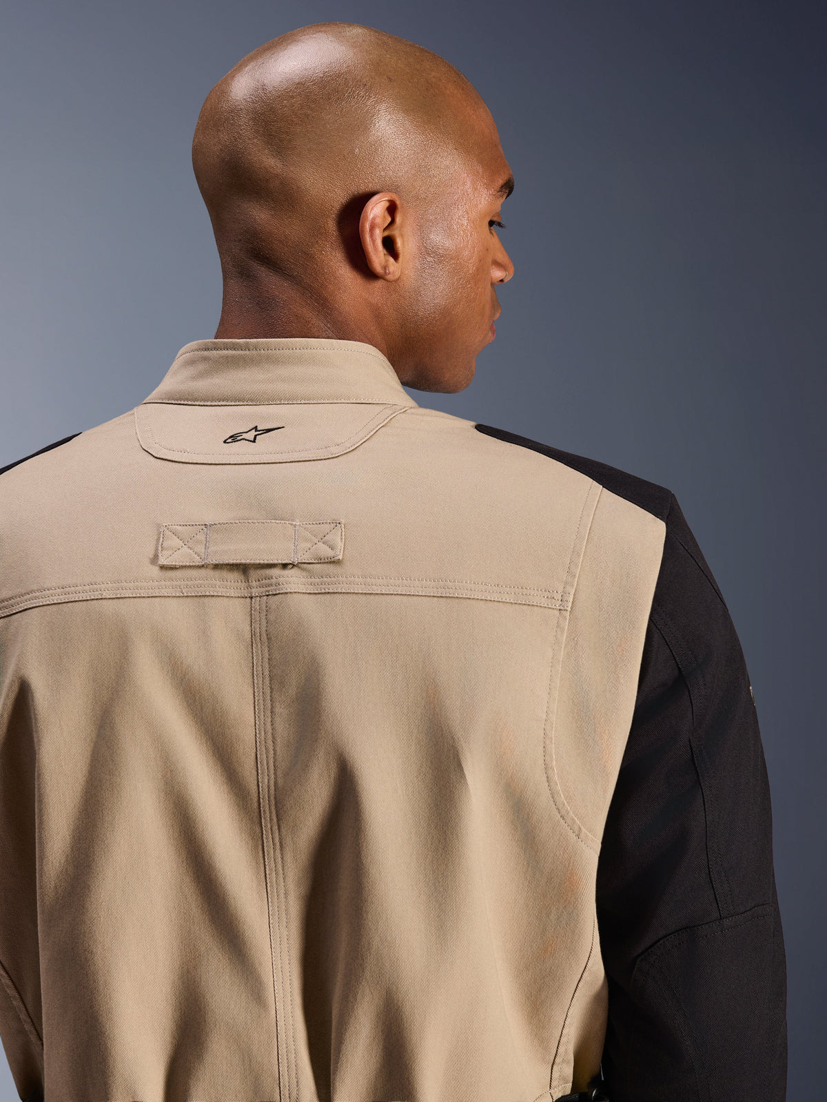 Alpinestars Dice Jacket, urban motorcykeljakke, tan og sort, tætbillede af krave og skulder på ryggen, broderet logo, robust polybomulds-twill-konstruktion, gadeklar arbejdstøjsstil.