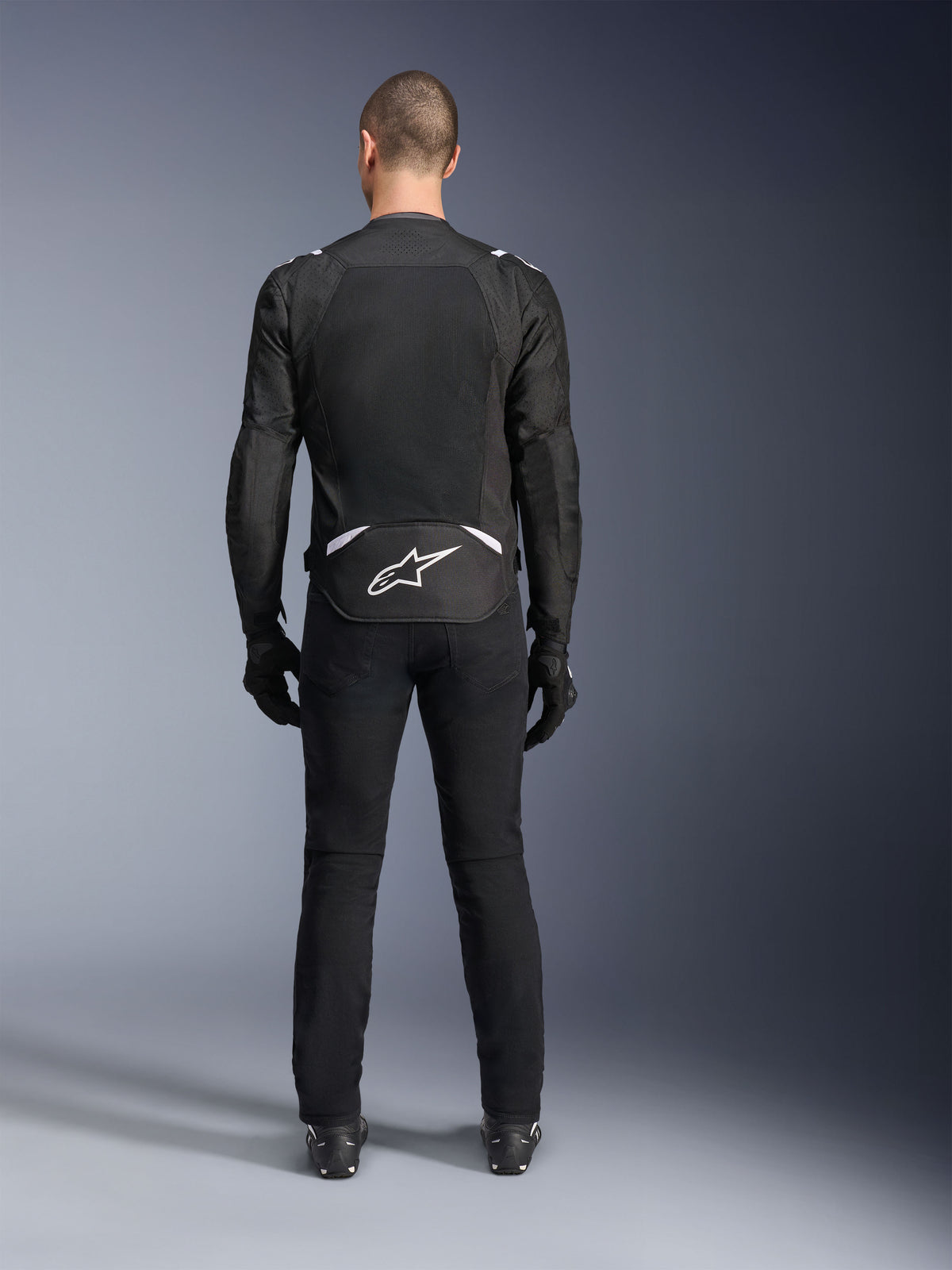 Alpinestars T-Sps Air V2 Jacket, Rear View, Black and White textile motorcycle jacket, featuring a large mesh back panel for maximum airflow and white Astars logo on the lower back, worn with black riding pants and gloves