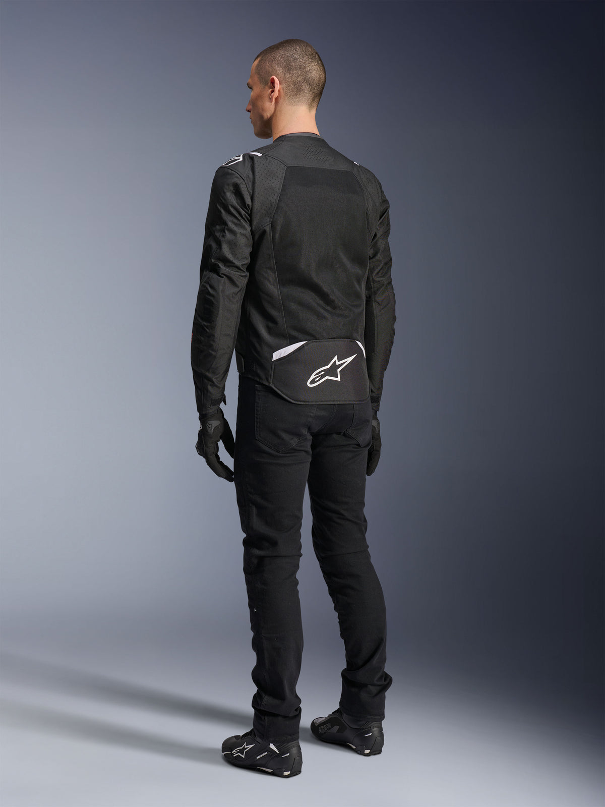 Alpinestars T-Sps Air V2 Jacket, Textile Motorcycle Jacket, Black, rear view showing large mesh ventilation panel and white Alpinestars logo on the lower back, paired with black riding pants and gloves for a sporty urban look.