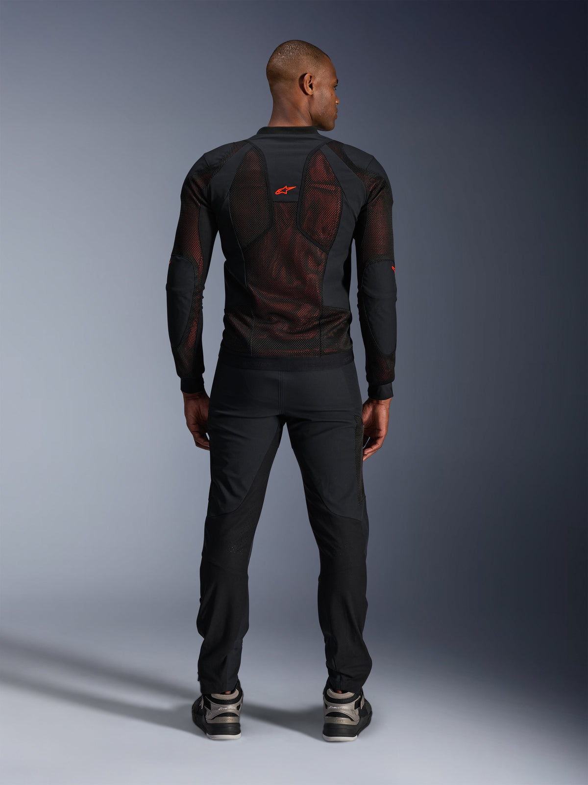 Alpinestars Troop-Air Pro Jakke i Sort Rød Fluo, set bagfra på model, teknisk pansret mesh-jakke med åndbare paneler, rødt logo på øverste del af ryggen, båret med sorte bukser og sneakers, urban motorcykelbeklædning