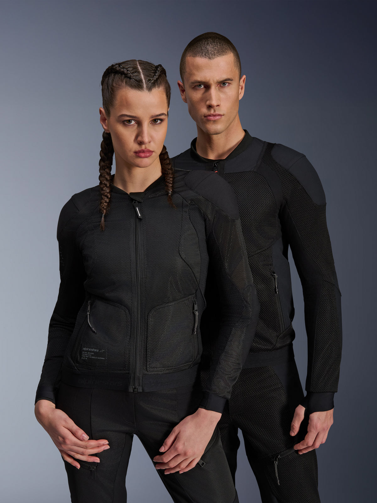 Mand og kvinde iført Alpinestars Troop-Air og Stella Troop-Air jakker, sorte tekniske mesh-motorcykeljakker, 2D tech mesh-struktur til ventilation og forstærkede paneler, moderne urbant køreudstyr