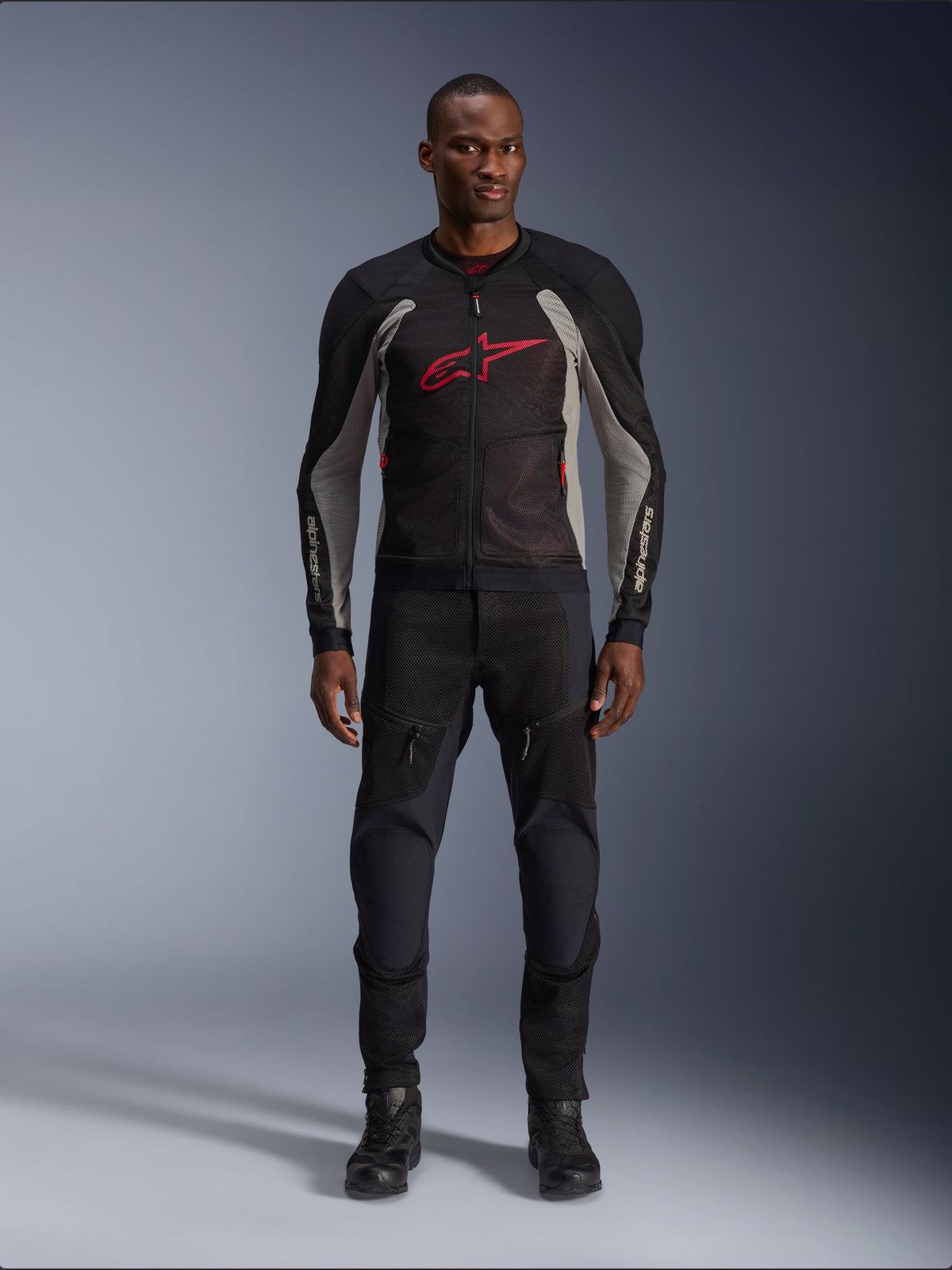 Mandlig model iført Alpinestars Troop-Air jakke i sort, askegrå og klar rød, teknisk mesh-motorcykeljakke med et markant rødt logo på brystet, kombineret med sorte motorcykelbukser og støvler, urbant motorcykeludstyr til vejbrug