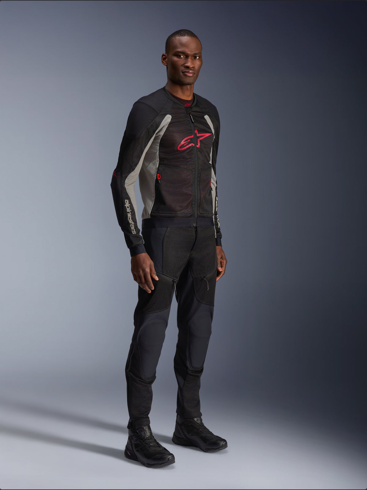 Alpinestars Troop-Air-jakke, teknisk mesh-motorcykeljakke i sort, Ash Gray og Bright Red, båret af en model med matchende sorte bukser og støvler, med et rødt Alpinestars-logo på brystet, urbant og moderne køreudstyr
