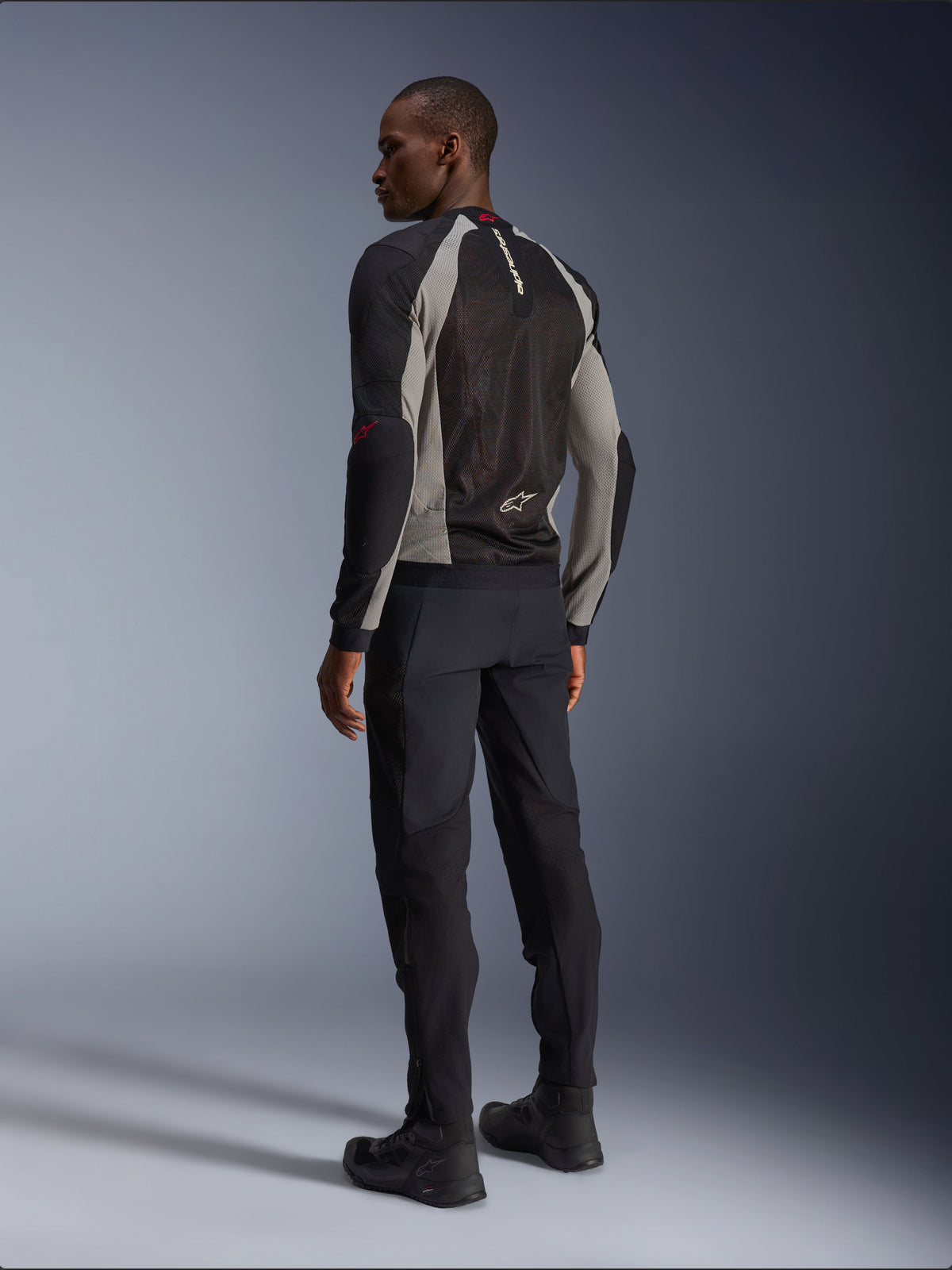 Model iført Alpinestars Troop-Air-jakke set bagfra, Black Ash Gray og Bright Red-detaljer, teknisk mesh-konstruktion for ventilation, kombineret med sorte motorcykelbukser og kørestøvler, urban contemporary-stil