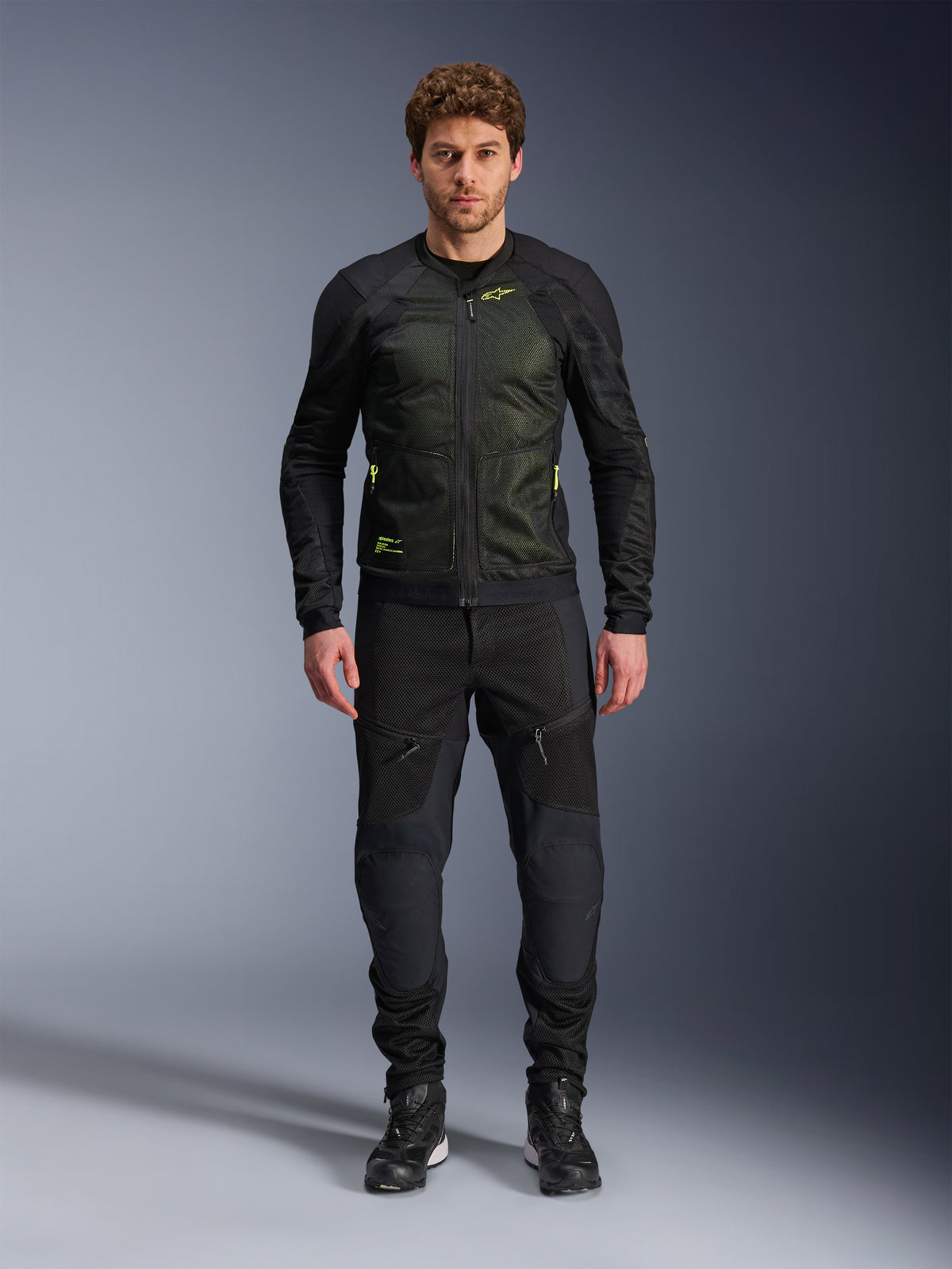 Mandlig model iført Alpinestars Troop-Air-jakke i Black Yellow Fluo, med tekniske mesh-paneler og klare gule detaljer, kombineret med sorte kørebukser og sko, moderne motorcykelbeklædning til varmt vejr