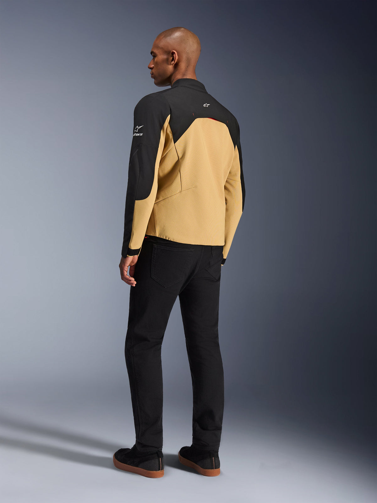 Alpinestars Provoke jakke, urban motorcykeljakke i Black Camel, set skråt bagfra, camel-farvet krop med sorte skulder- og ærmepaneler, hvide Alpinestars-logoer, båret med sorte bukser, moderne teknisk køreudstyr