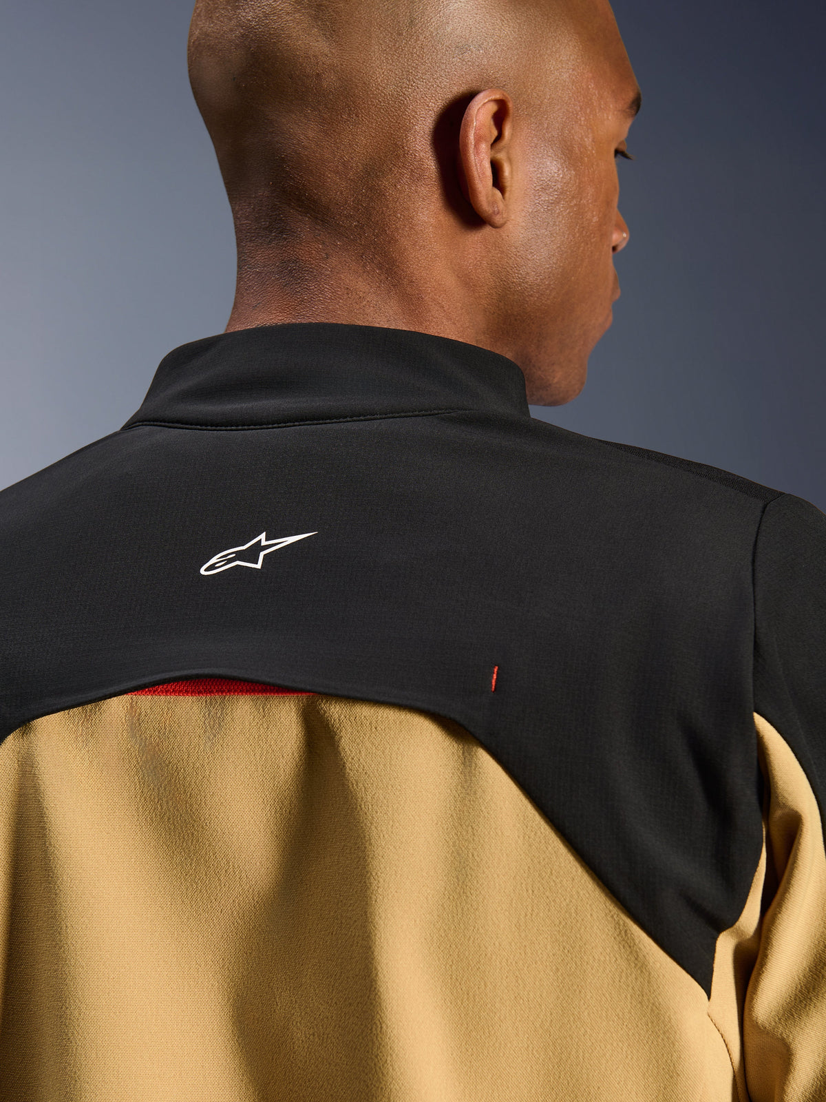 Alpinestars Provoke Jakke, urban motorcykeljakke, sort og camel, nærbillede af det øverste af ryggen og kraveområdet med et hvidt Astars-logo på et sort bærestykke og camel-farvede paneler forneden, moderne outdoor-inspireret teknisk design