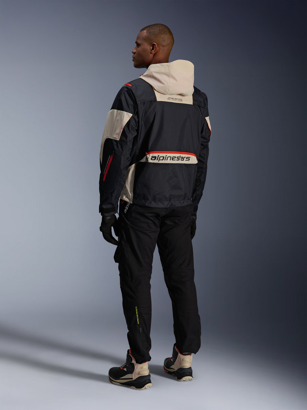 Alpinestars Mogress Air-jakke, sort og mandelfarvet urban motorcykeljakke med orange detaljer, set bagfra.