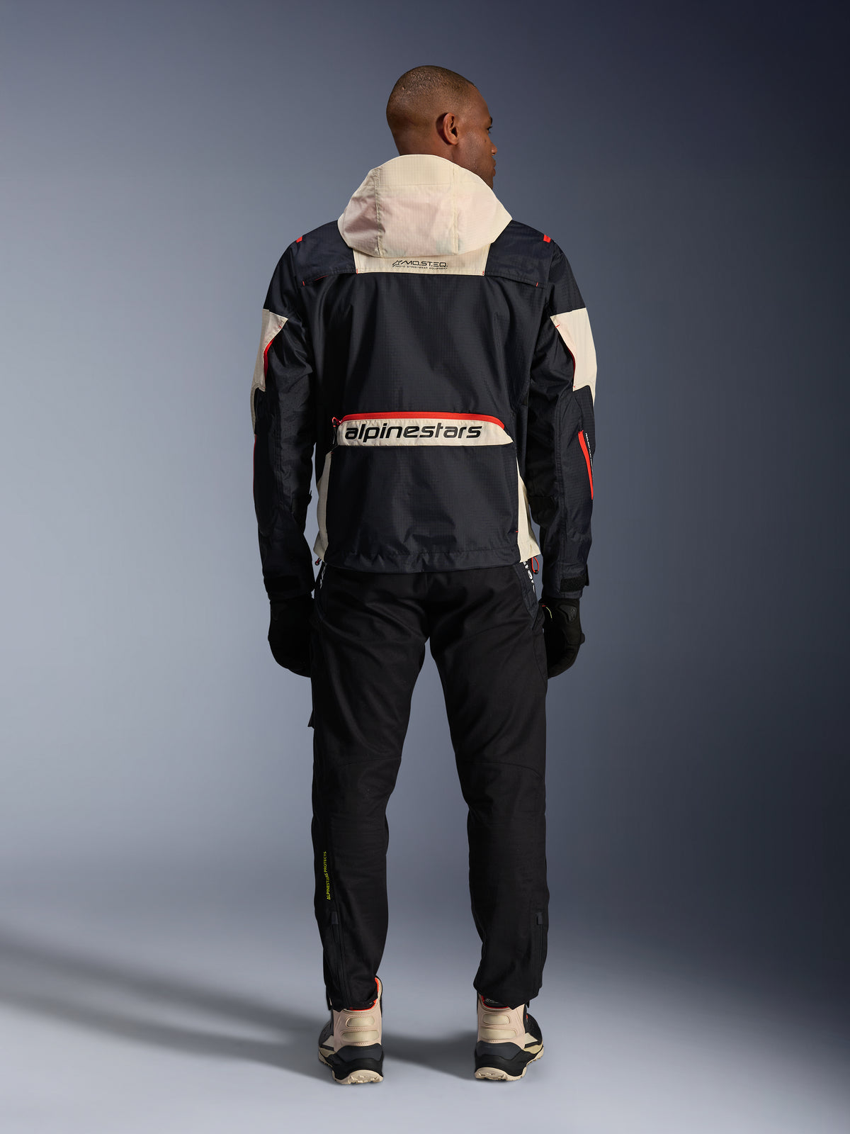 Alpinestars Mogress Air urban motorcykeljakke til herrer, sort og orange med creme hætte, set bagfra.