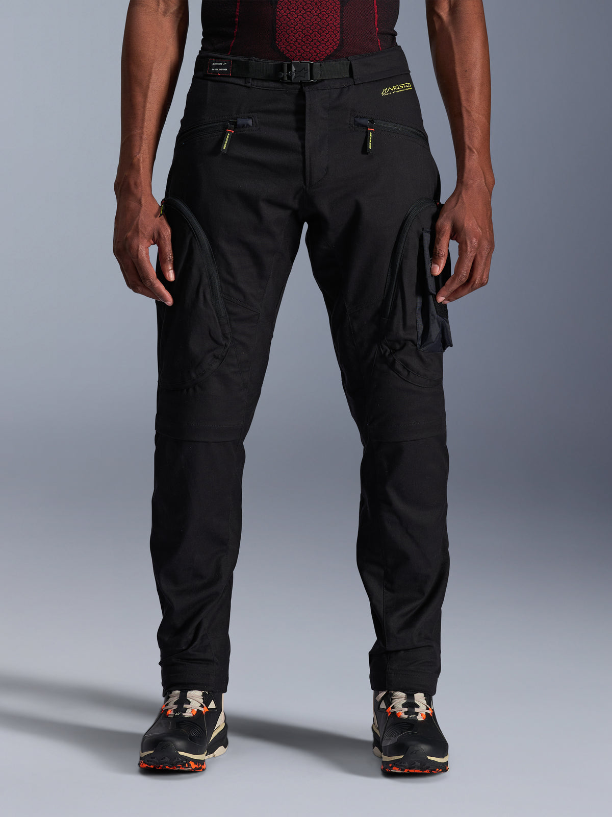 Alpinestars Acteon bukser, sorte urban motorcykelbukser, tapered regular pasform med cargolommer i siden og omvendte lynlåse, integreret bælte og gult logo, beskyttende tekstil-køreudstyr