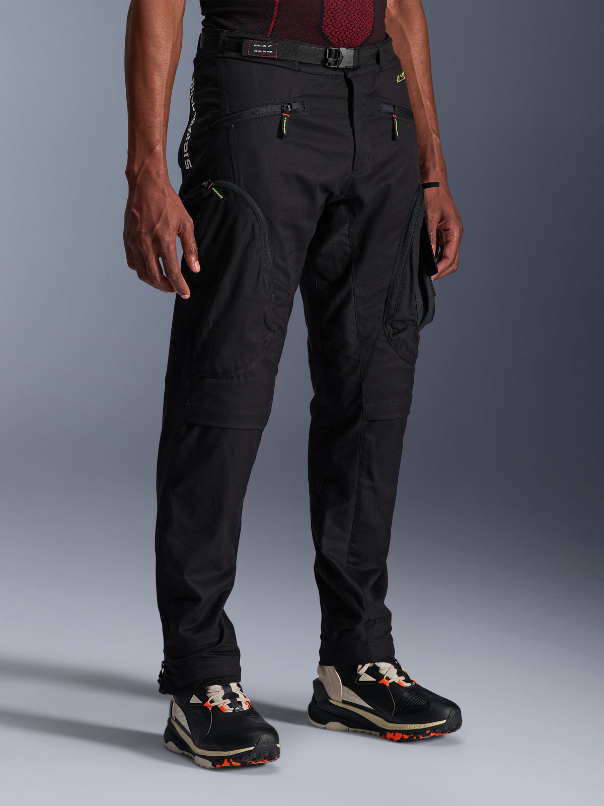 Alpinestars Acteon bukser, sorte motorcykelbukser, vist på en model, med en moderne tilspidset silhuet, cargolommer med lynlås, justerbart taljebælte og tekniske sneakers, urbant køreudstyr