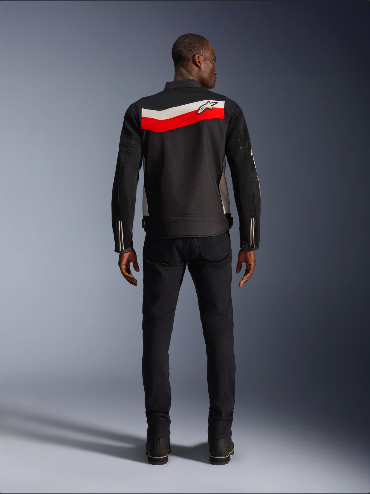 Alpinestars T-Dyno Air Jakke, tekstil motorcykeljakke til mænd, set bagfra, sort med klare røde og ecru vandrette striber over ryggen, Alpinestars-logo på bærestykket, båret med sorte bukser og støvler, åndbar 3D-mesh-konstruktion
