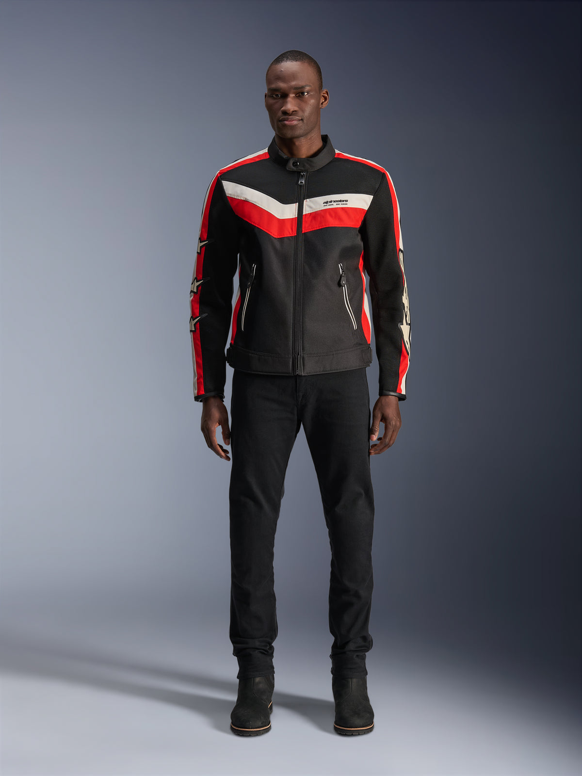 Alpinestars T-Dyno Air jakke, tekstil motorcykeljakke, sort, rød og ecru, båret af en model med sorte bukser og støvler, med et vintage-inspireret design med markante farvestriber på brystet, stjernelogoer på ærmerne og åndbar mesh-konstruktion til bykørsel.