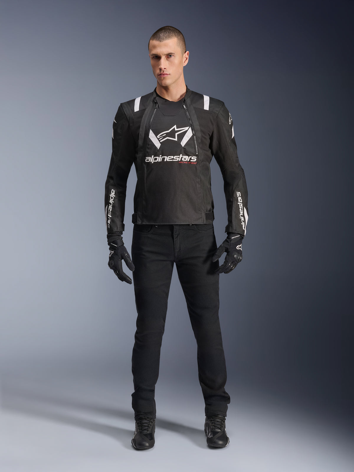 Alpinestars T-Stunt Air Jacket, sort og hvid motorcykeljakke, båret med sorte kørebukser, handsker og støvler, med markant hvidt Alpinestars-branding på brystet og ærmerne, sport-cut tekstildesign med mesh-paneler til ventilation