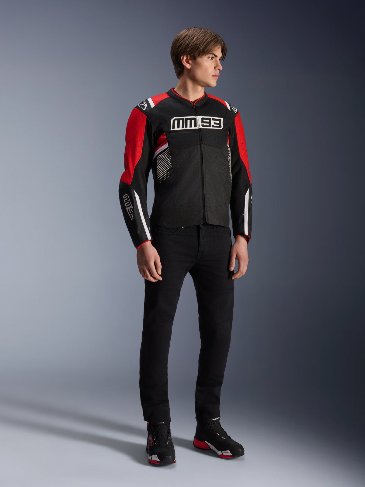 Mandlig model iført Alpinestars MM93 T-SPS Air v2-jakken i Black Bright Red White, med fremtrædende MM93-branding på brystet og ærmerne, kombineret med sorte bukser og motorcykelstøvler, sporty urban motorcykelstil med synlige mesh-paneler for luftgennemstrømning.