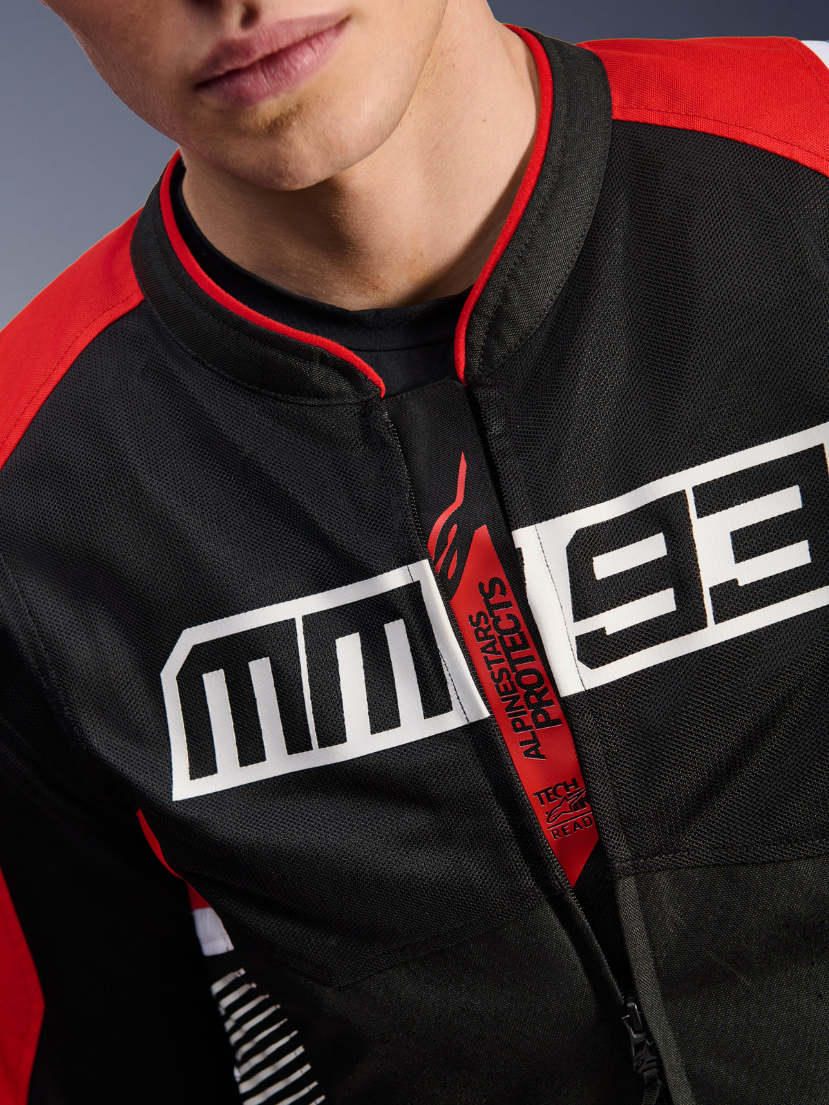 Alpinestars MM93 T-SPS Air V2 jakke, motorcykeljakke, sort, klar rød og hvid, tætbillede af brystet med stort hvidt MM93-logo, rød 'Alpinestars Protects' og 'Tech-Air Ready' lynlåsstrop, tech mesh-tekstur