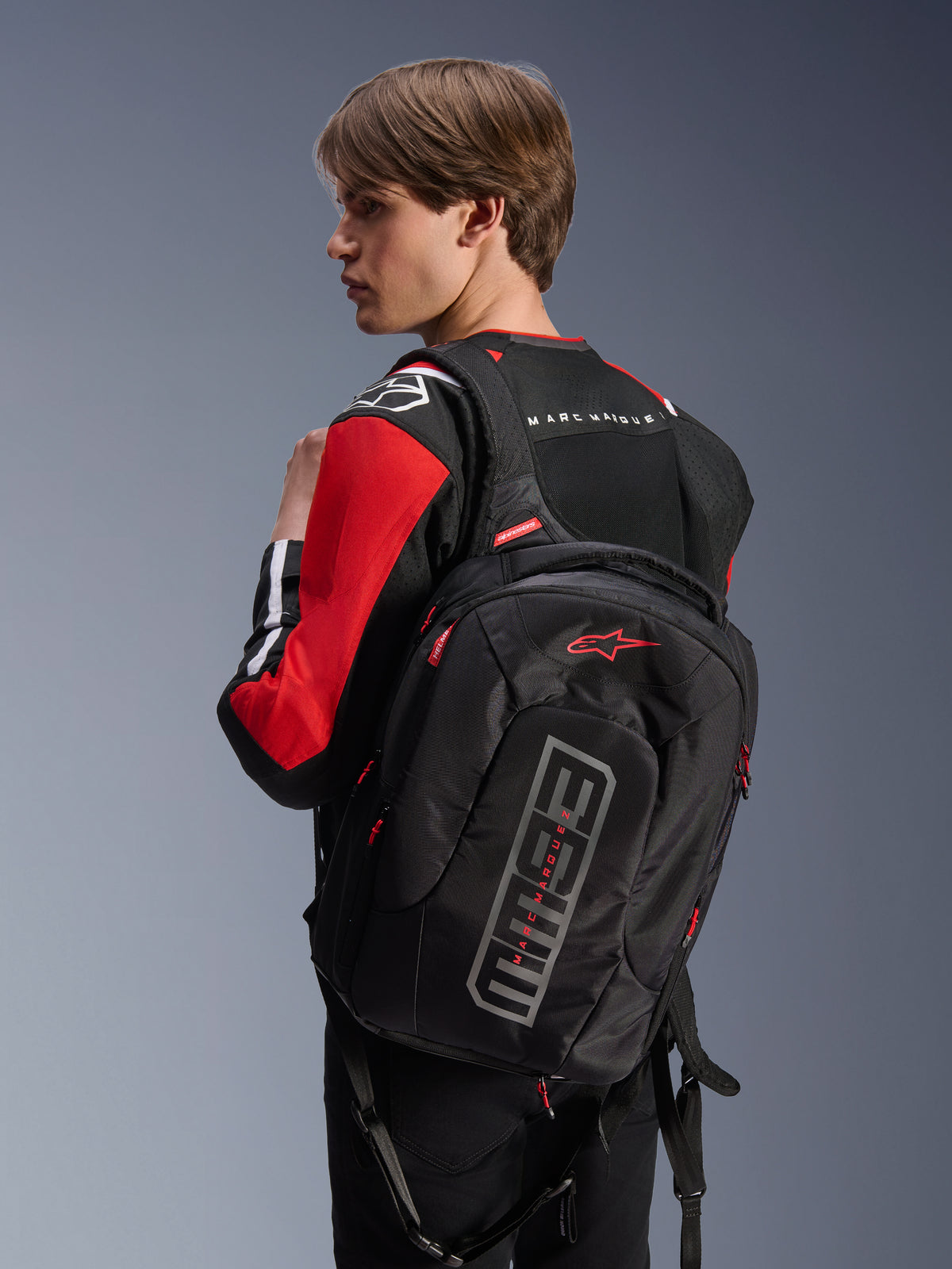 Alpinestars MM93 City Hunter V2 rygsæk, sort, med rødt Astars-logo og grå MM93-branding, båret af en kører i en rød og sort motorcykeljakke, urbant køreudstyr fra Marc Márquez-kollektionen