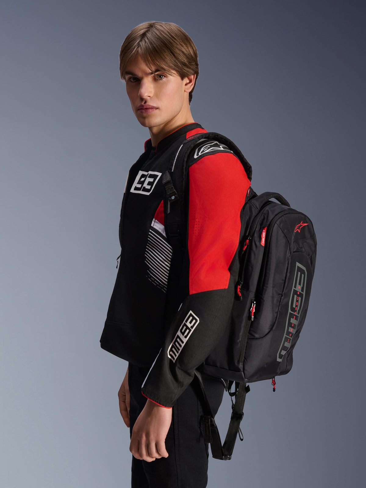 Alpinestars MM93 City Hunter V2 rygsæk, sort med røde detaljer, båret af en model i en matchende sort og rød MM93 motorcykeljakke, med Marc Márquez-branding og logoer, urban køreudstyr