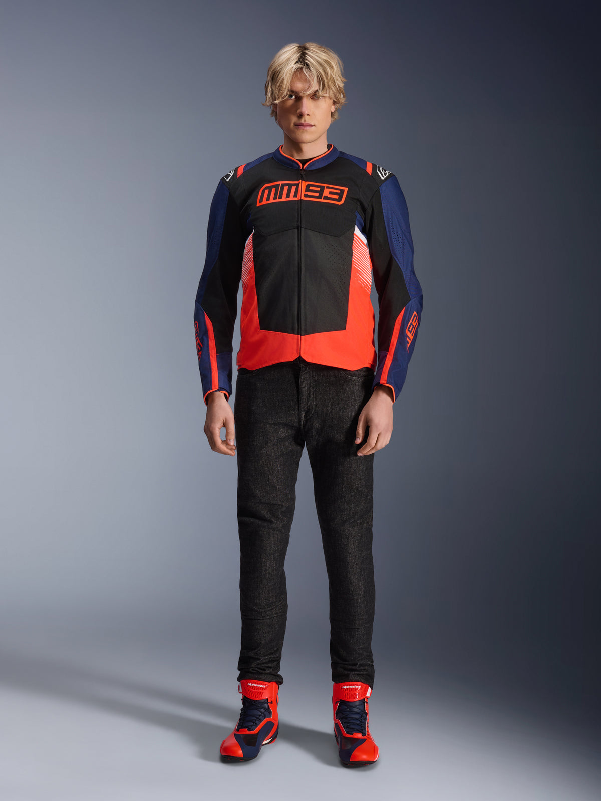Alpinestars MM93 T-SPS Air V2 jakke, mørkeblå og sort med fluorescerende røde detaljer, med det karakteristiske MM93-logo på brystet, båret med sorte kørebukser og matchende blå og røde støvler, urbant motorcykeloutfit