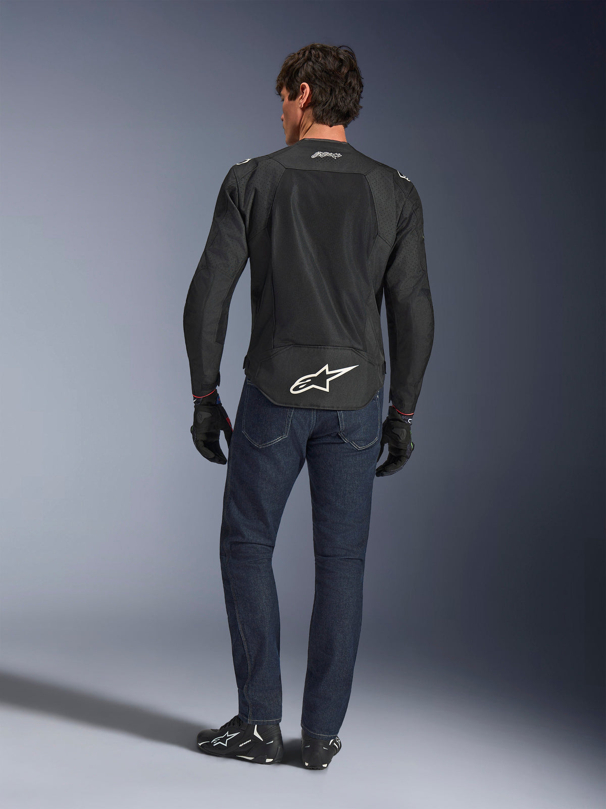 Alpinestars FQ20 T-SPS Air V2 Monster Jakke, sort, set bagfra på model iført mørkeblå jeans og sorte motorcykelstøvler, med et stort hvidt logo på den nedre ryg og åndbare mesh-paneler, urbant sports-køreudstyr