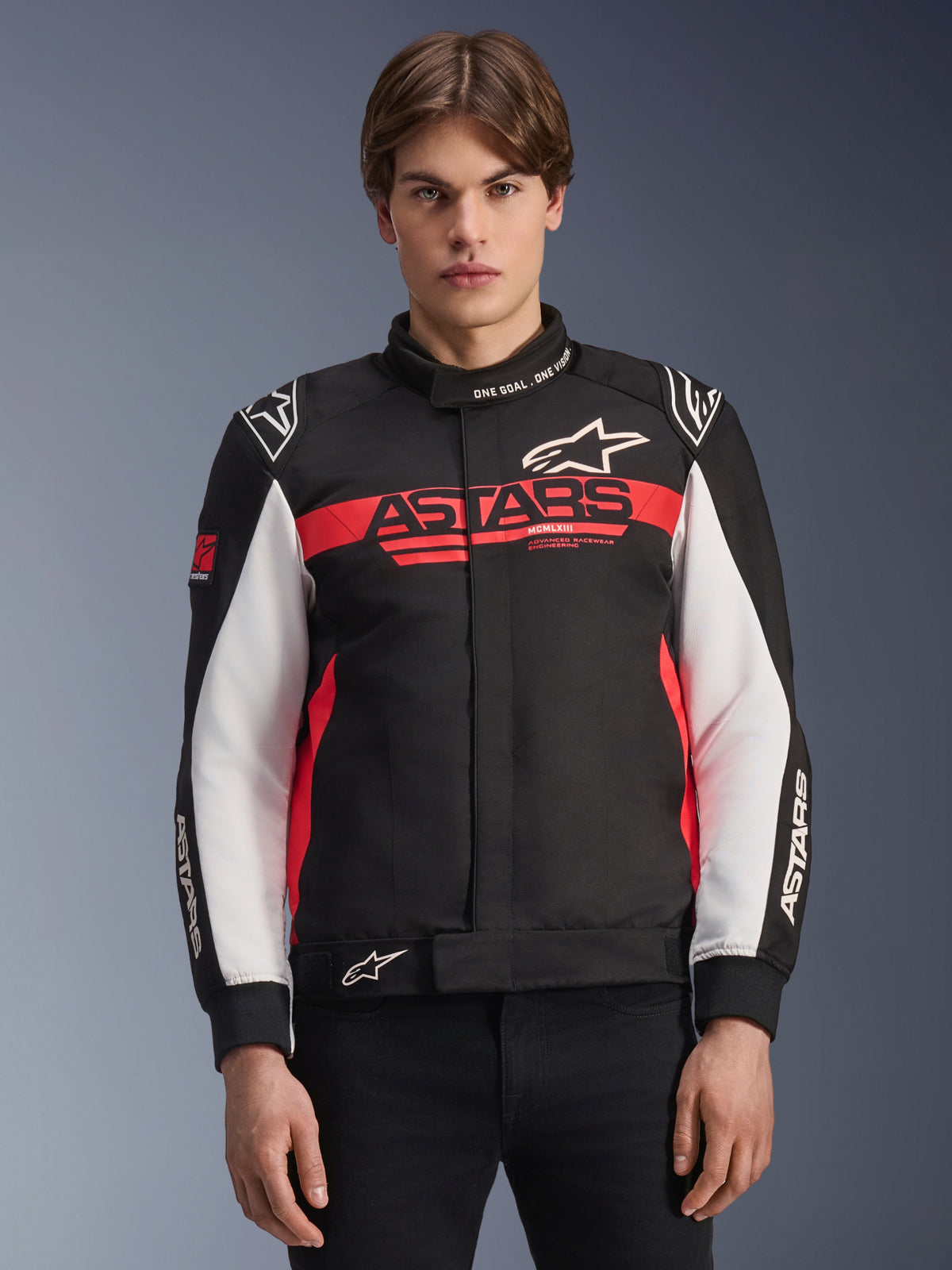 Alpinestars Monza Sport-jakke, motorcykeljakke i tekstil, sort med klar rød og hvid, med markant ASTARS-logo på brystet, 'ONE GOAL. ONE VISION.'-tekst på kraven, hvide ærmepaneler og stjernelogoer, båret af en model mod en tonet baggrund