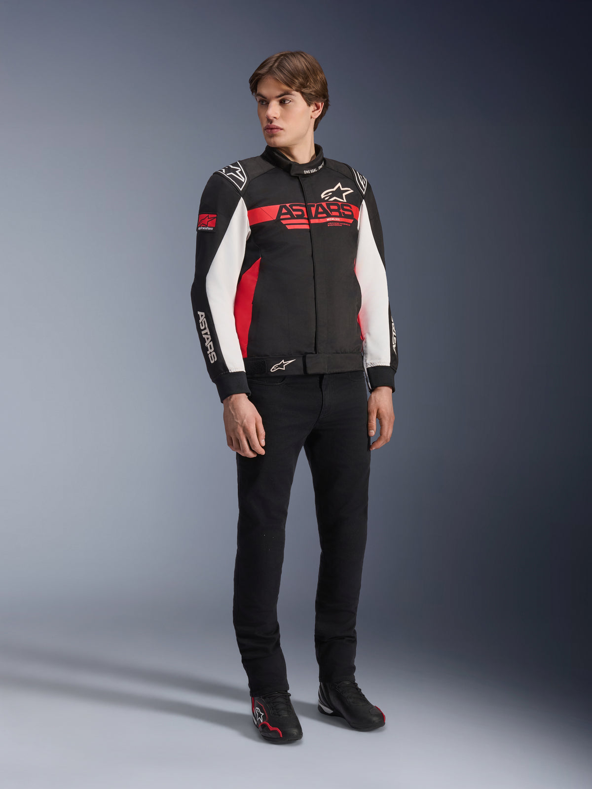 Alpinestars Monza Sport jakke, sort, lys rød og hvid, tekstil motorcykeljakke, racerinspireret design med ASTARS-branding på bryst og ærmer, båret af en model med sorte bukser og køresko, afslappet sportskøreudstyr