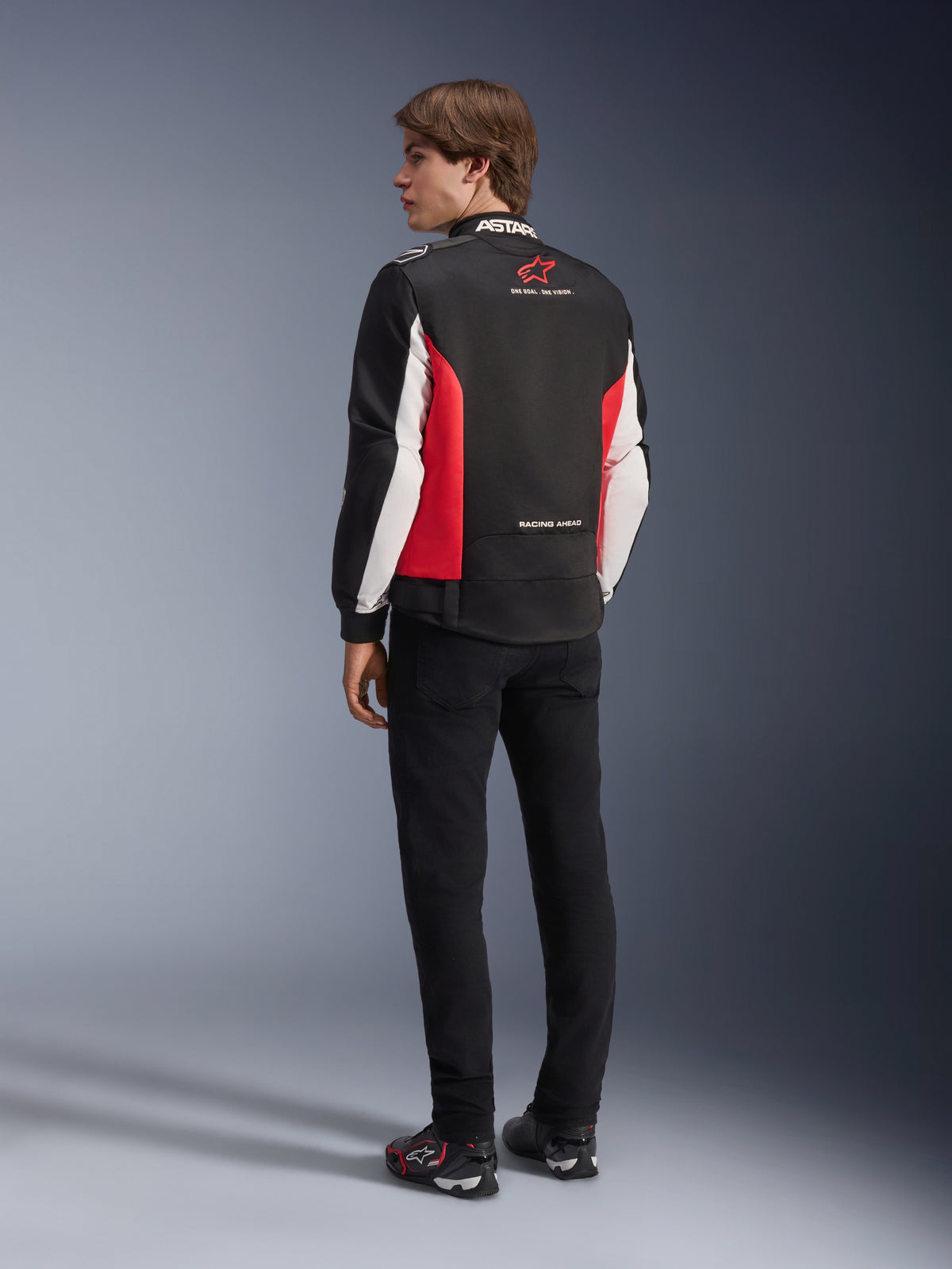 Alpinestars Monza Sport jakke, tekstiljakke til motorcykel, sort, klar rød og hvid, rygvisning af model med røde sidepaneler og hvide detaljer på ærmerne, Alpinestars logo og 'ONE GOAL. ONE VISION.' tekst, parret med sorte bukser og køresko for et sportsinspireret look
