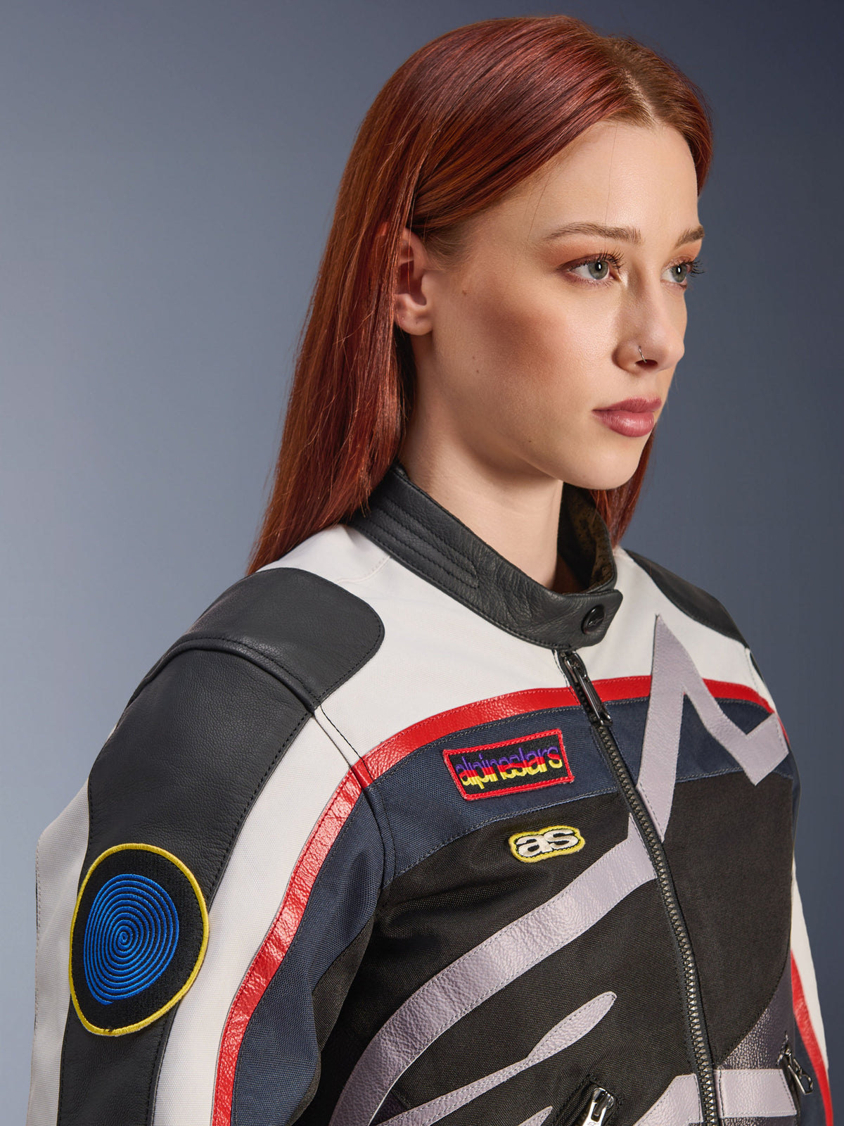 Alpinestars Idles Women’s Jacket, Off White, Flame Red and Black, featuring vintage-inspired racing patches and a wrap-around logo, textile and leather construction, urban motorcycle style worn by a model.