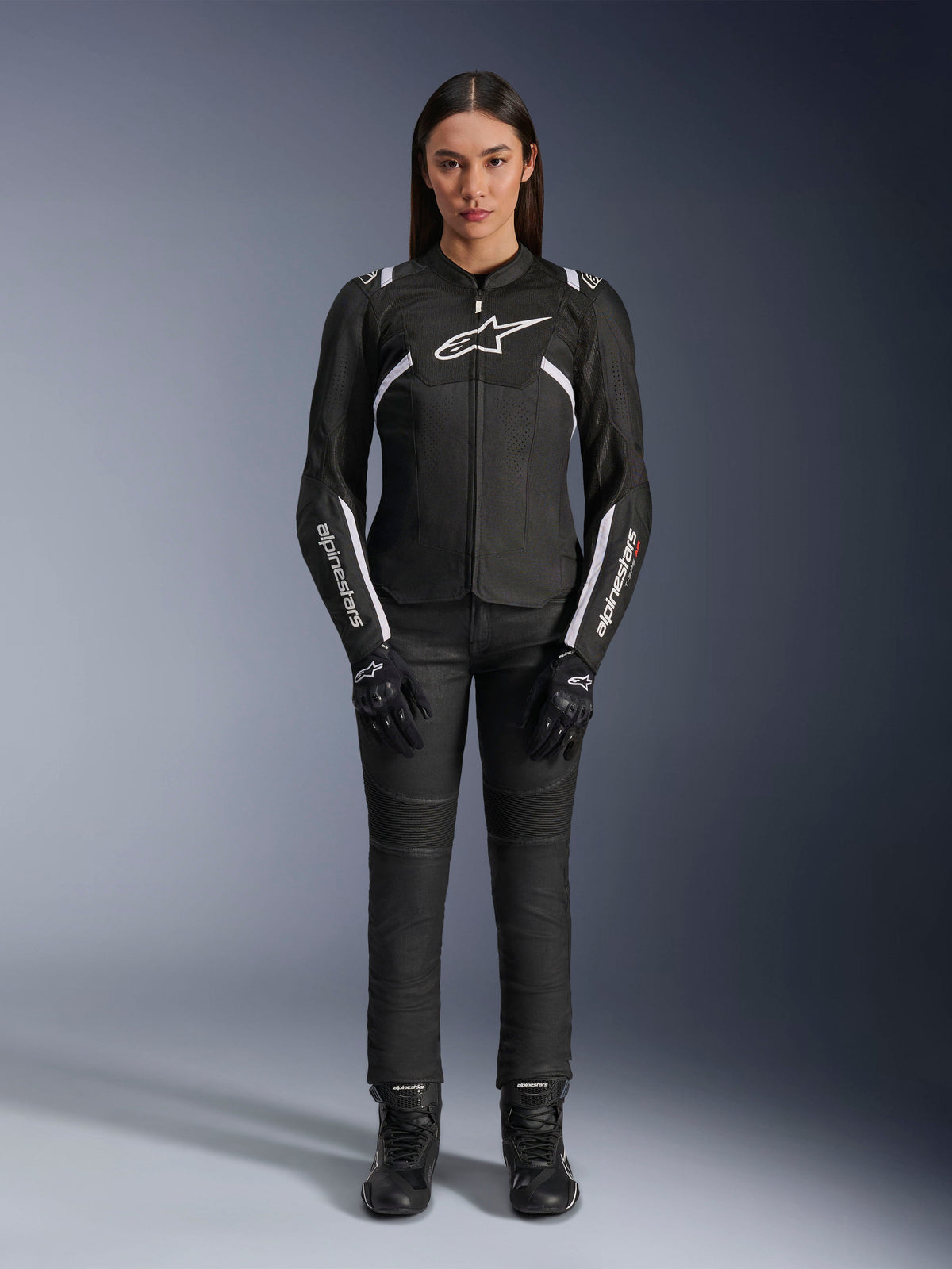 Alpinestars Stella T-Sps Air V2-jakke, motorcykeljakke til kvinder, sort og hvid, med mesh-paneler og hvide detaljer, båret med sorte bukser, handsker og støvler, atletisk pasform til bykørsel