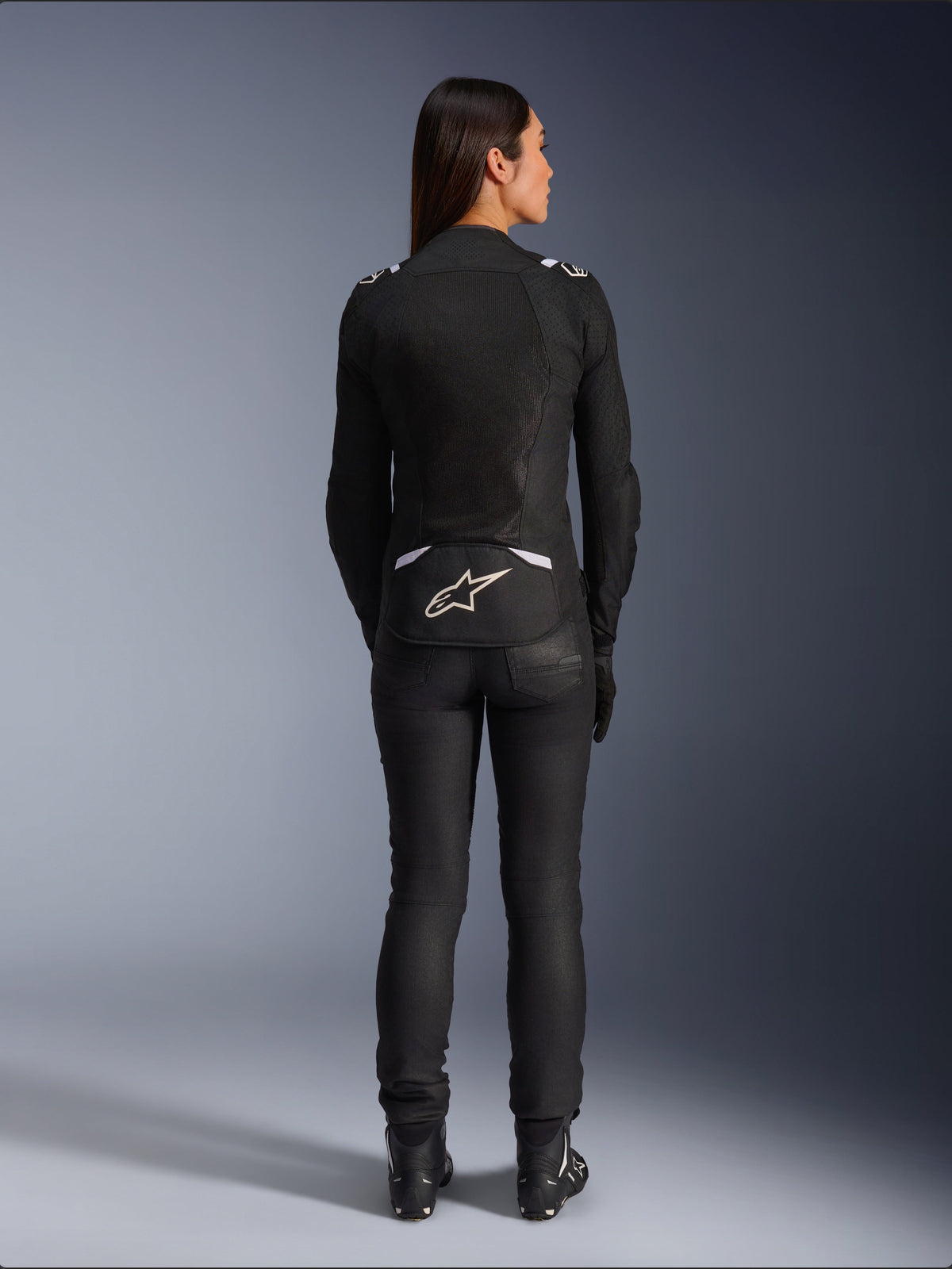 Alpinestars Stella T-SPS Air v2 jakke, motorcykeljakke i tekstil til damer, sort og hvid, set bagfra med mesh-ventilationspaneler og hvidt logo på lænden, båret med sorte kørebukser og støvler, urbant sportsudstyr