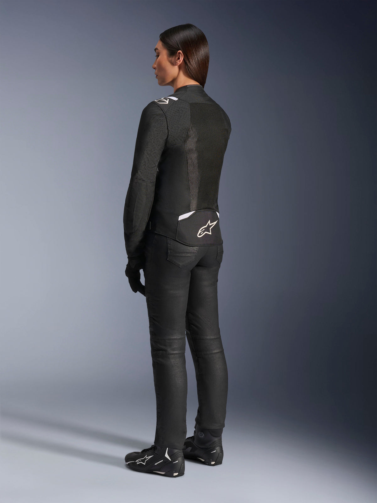 Alpinestars Stella T-Sps Air V2 jakke, sort og hvid, set bagfra med mesh-paneler og logo på den nederste del af ryggen, kombineret med sorte kørebukser og motorcykelsko, sportsligt tekstiludstyr til kvinder