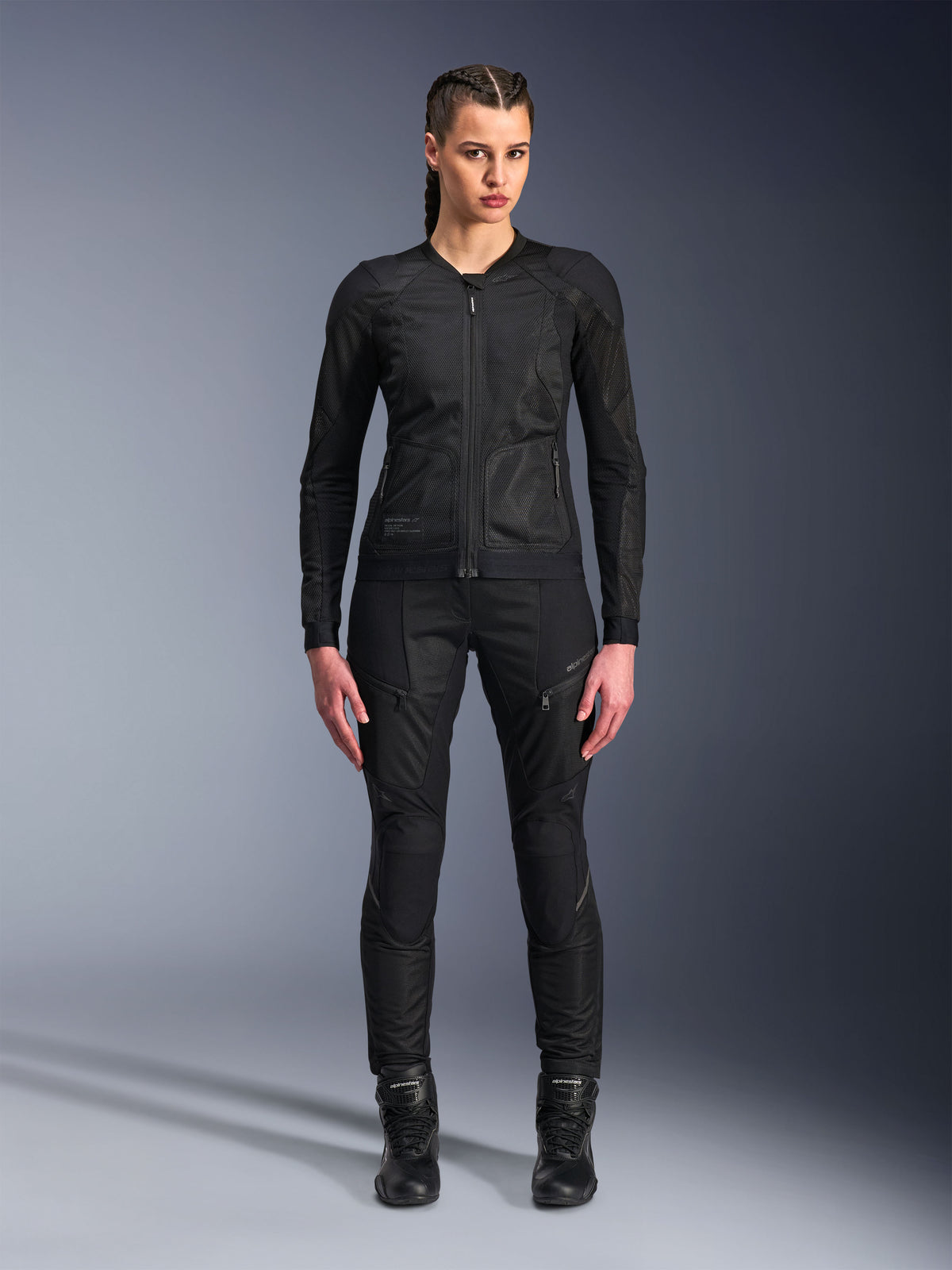 Alpinestars Stella Troop-Air jakke, motorcykeljakke til damer, sort, teknisk 2D mesh-konstruktion med et minimalistisk design, båret med sorte kørebukser og støvler, moderne urban motorcykelstil.