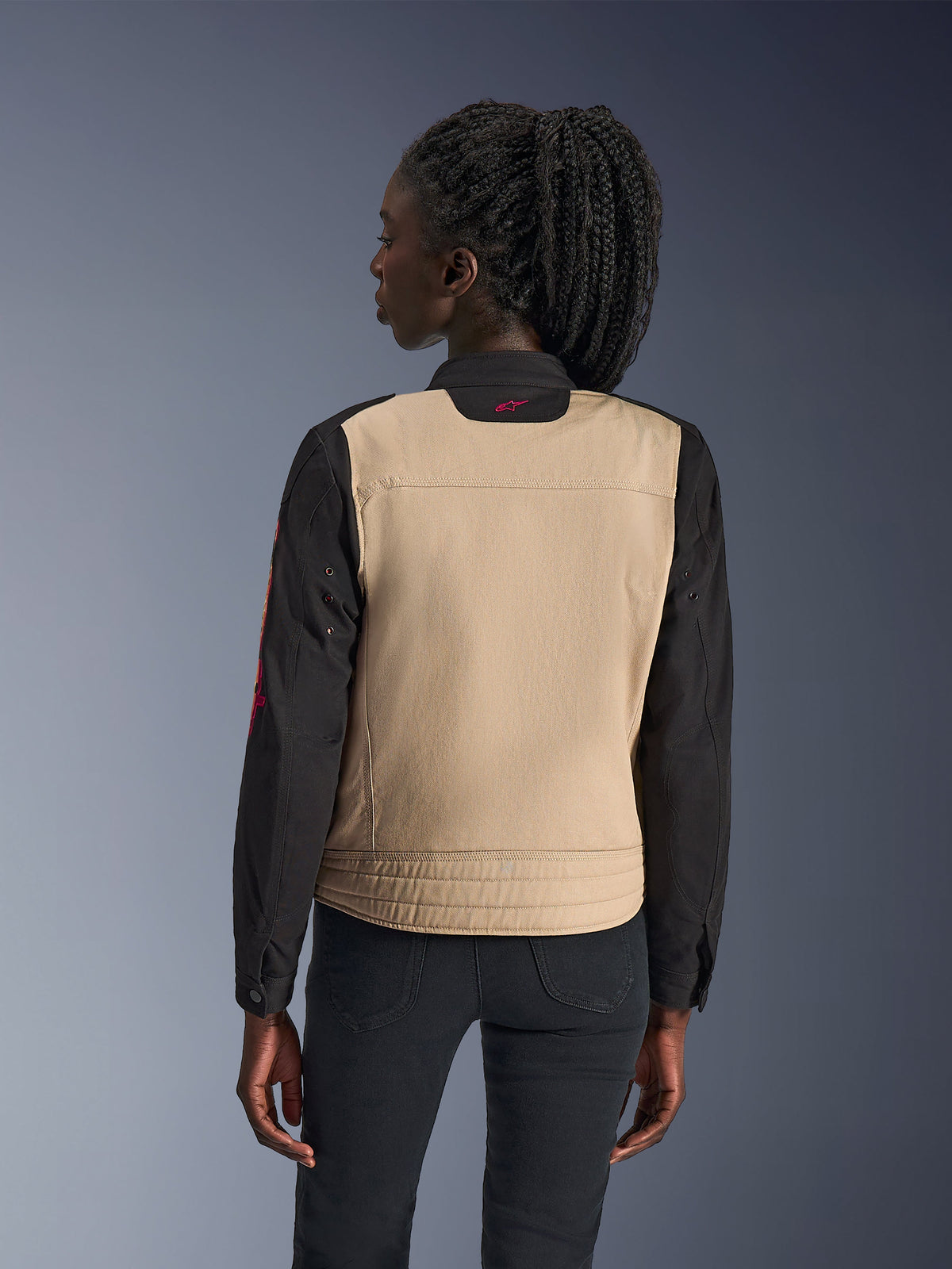 Alpinestars Woman Stella Grace Jacket, urban motorcycle jacket, Aluminum and Black, back view showing a tan back panel and black sleeves, workwear-inspired design with a small pink logo on the collar, paired with dark pants