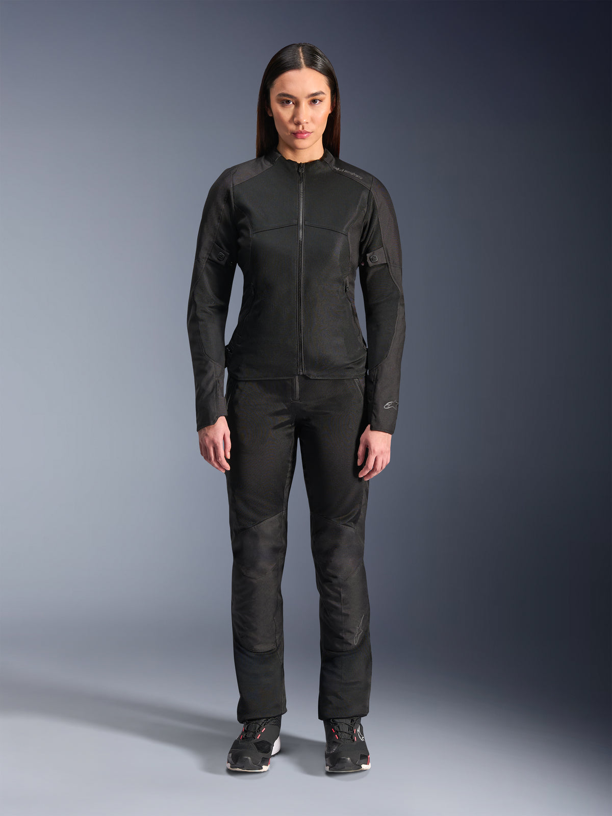 Kvinde iført Alpinestars Stella C-1 Air Jakke i sort, kombineret med matchende sorte tekstil-motorcykelbukser og køresko, med et stilrent urbant design med store mesh-paneler for luftgennemstrømning.