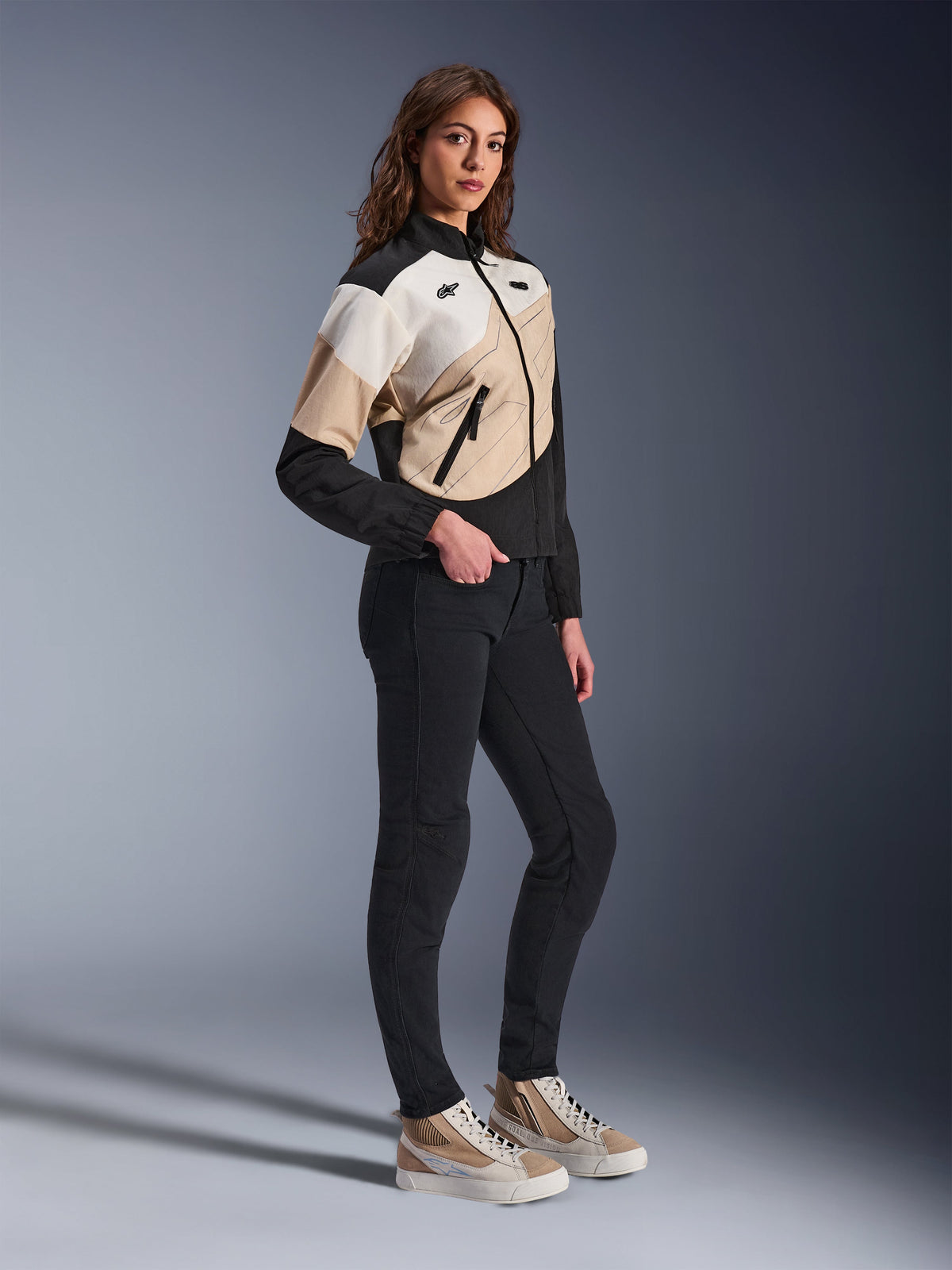 Alpinestars Stella Moshell Jacket, Women's Urban Motorcycle Jacket, Black Sand and Off White, featuring an asymmetrical geometric design, worn with slim black pants and tan sneakers, full-length studio shot for contemporary urban riding gear.