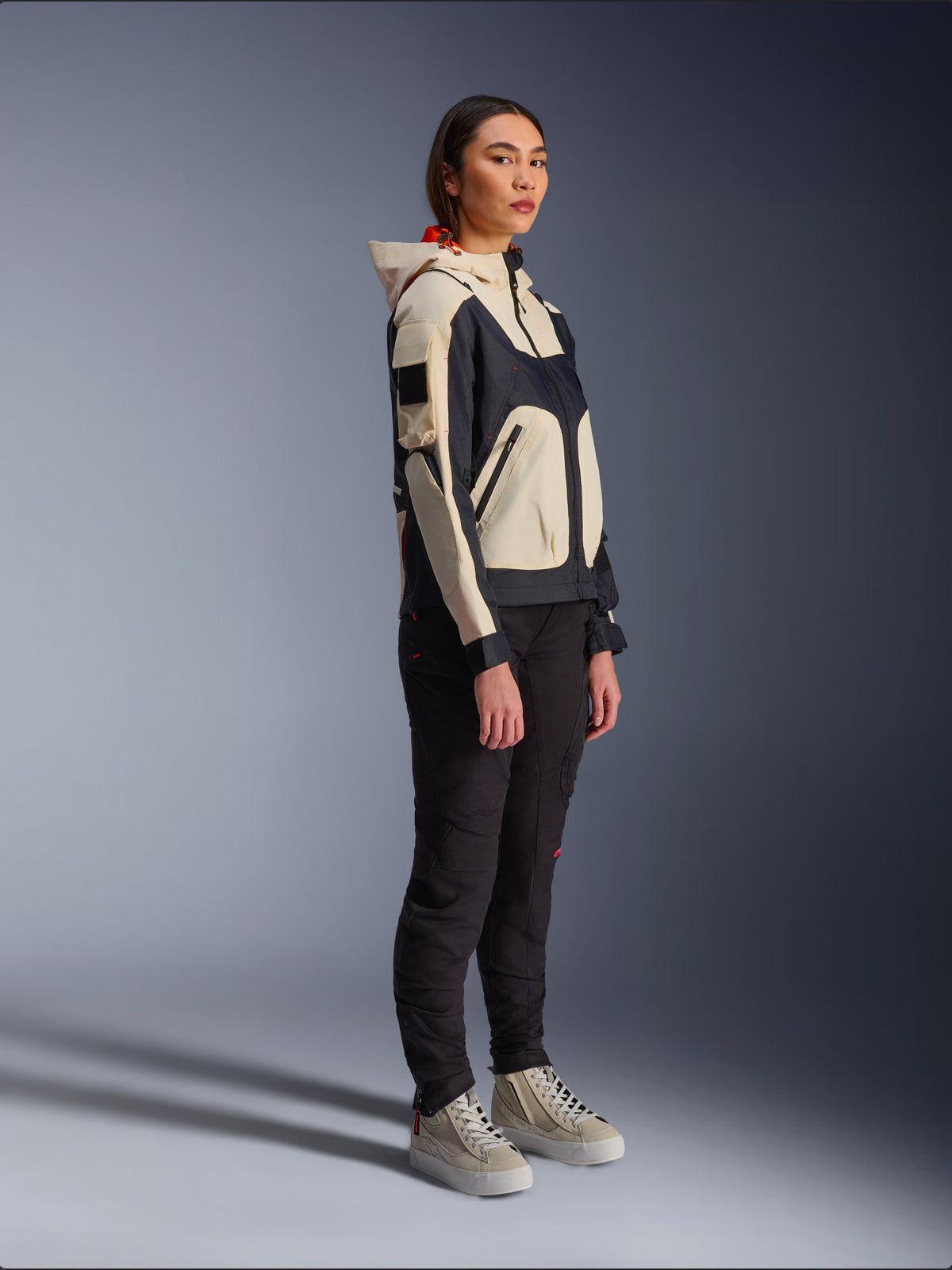 Alpinestars Molly Air Jacket in Black Almond, worn by a female rider with black pants and cream high-top sneakers, featuring a two-tone design with black and beige panels, integrated hood, and contemporary urban style.