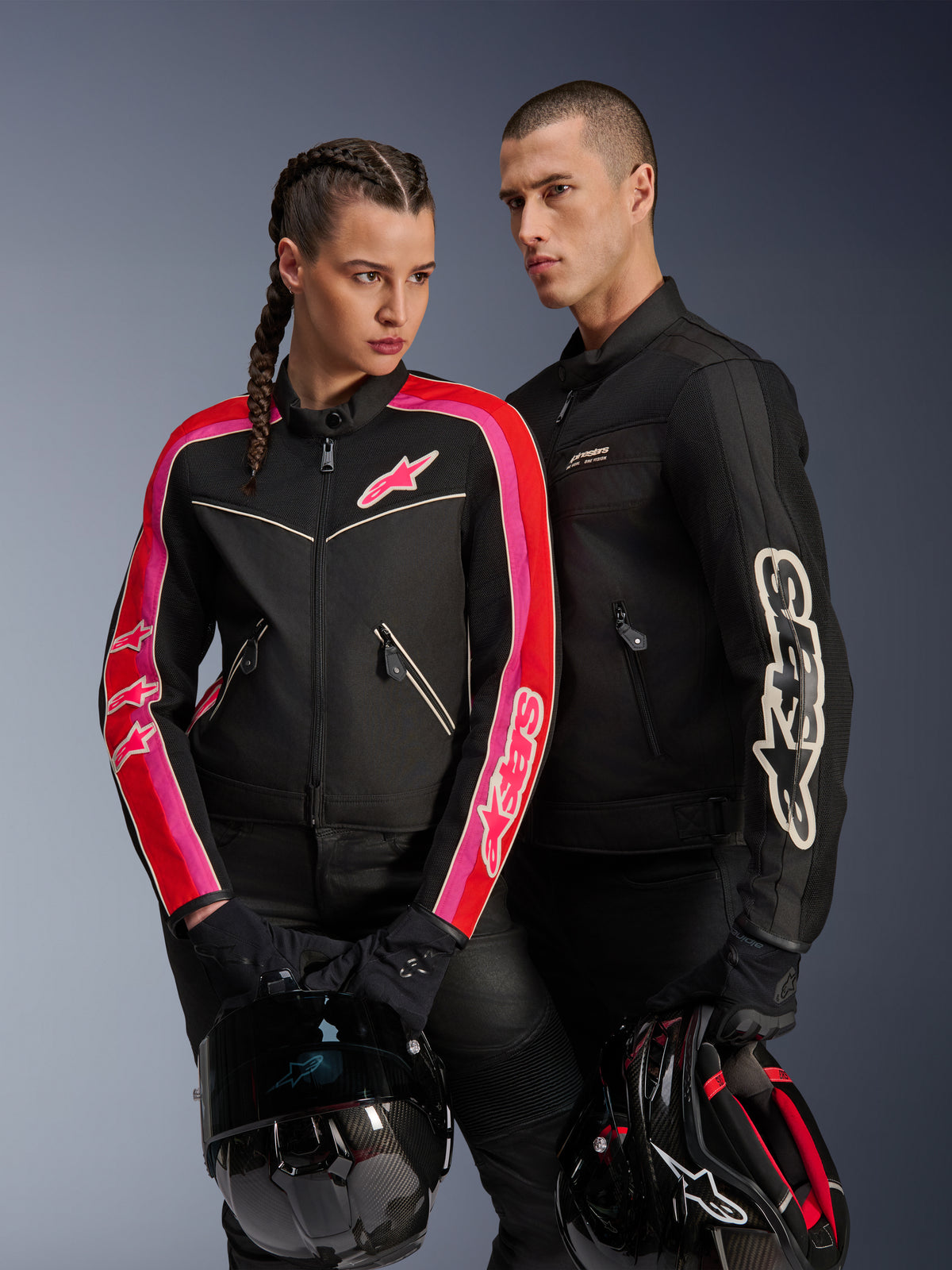 Alpinestars Stella T-Dyno Air-jakke på kvinde i sort, klar rød og fuchsia, parret med sort Dyno Air-jakke til mænd, begge kørere holder motorcykelhjelme, studieoptagelse af moderne urbant motorcykeludstyr