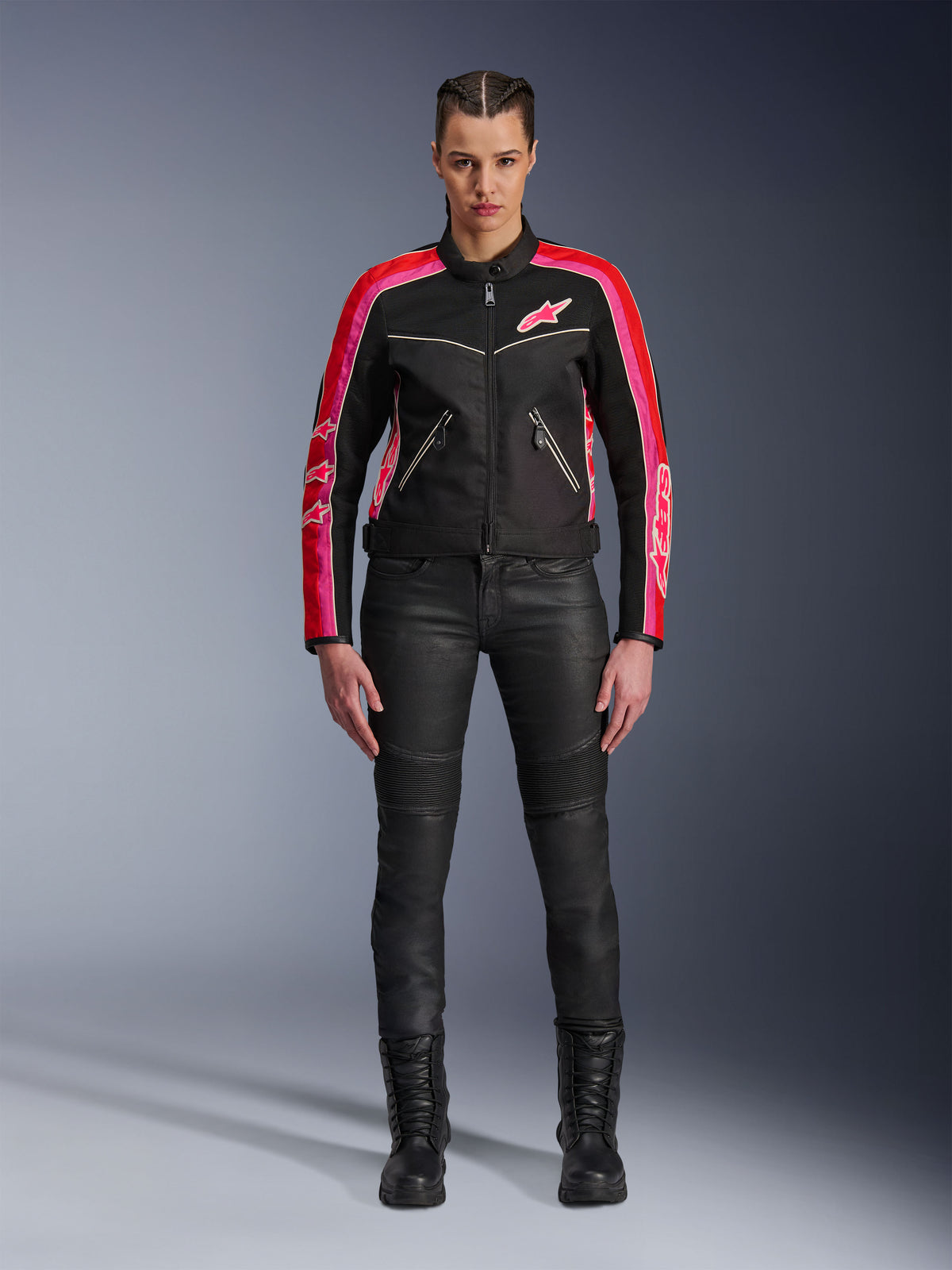 Kvindelig motorcyklist iført Alpinestars Stella T-Dyno Air-jakke, sort med klare røde og fuchsia-farvede detaljer, kombineret med sorte motorcykelbukser og snørestøvler, med 3D-meshpaneler, skræddersyet pasform og lyserøde stjernelogoer, urban motorcykeludstyr