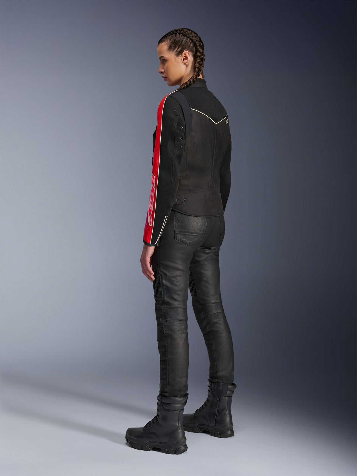 Kvinde iført Alpinestars Stella T-Dyno Air-jakke i Black Bright Red Fuchsia, kombineret med sorte motorcykelbukser og sorte støvler, set fra siden, hvilket fremhæver den røde og fuchsia grafik på ærmerne og den skræddersyede bikerpasform.