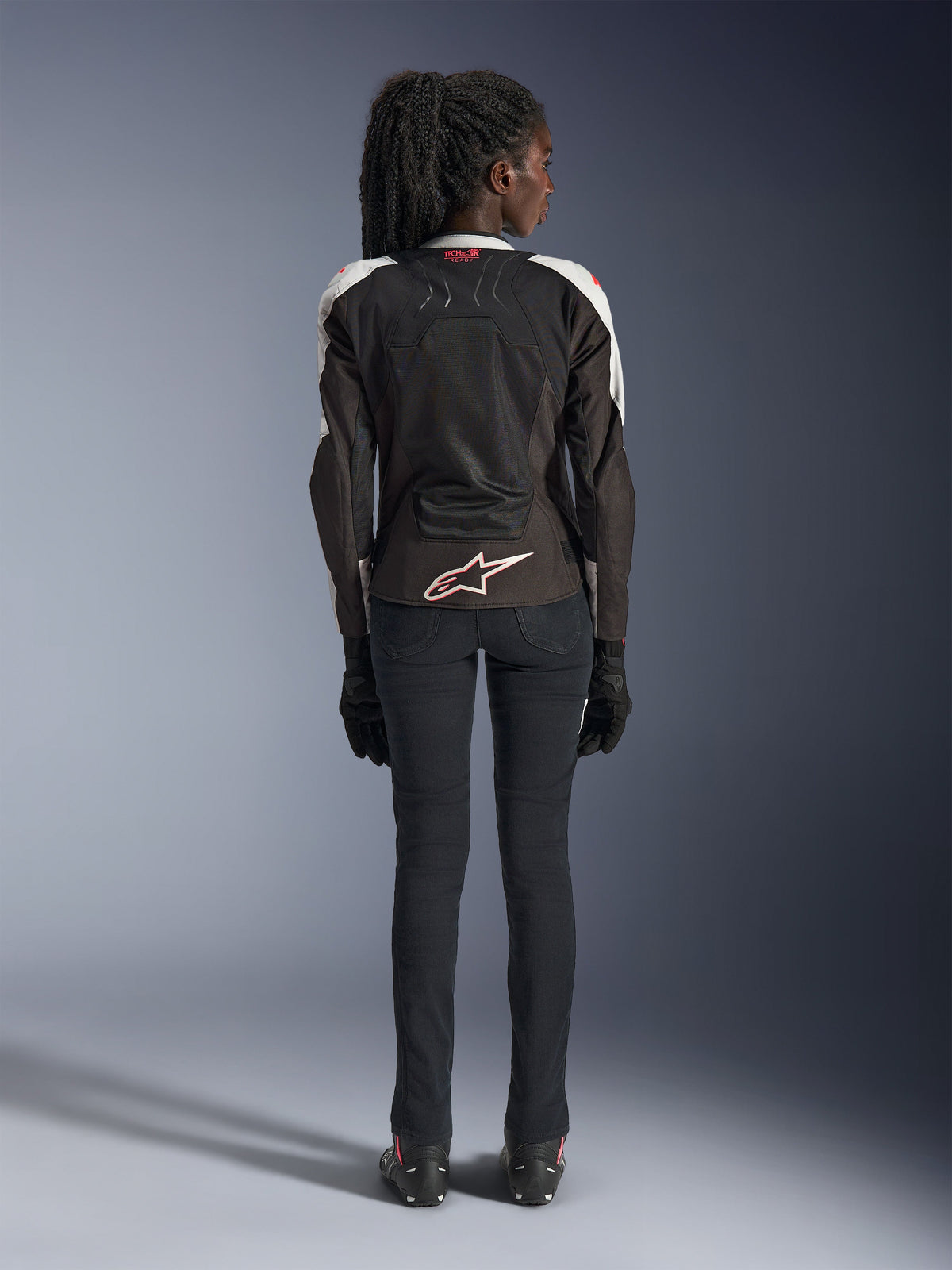 Alpinestars Woman Stella SMX Air-jakke, Ice Gray Black Coral Fluo, set bagfra med ventilerede mesh-paneler, hvidt Alpinestars-logo nederst på ryggen og Tech-Air Ready-branding ved kraven, vist med sorte motorcykelbukser og handsker.