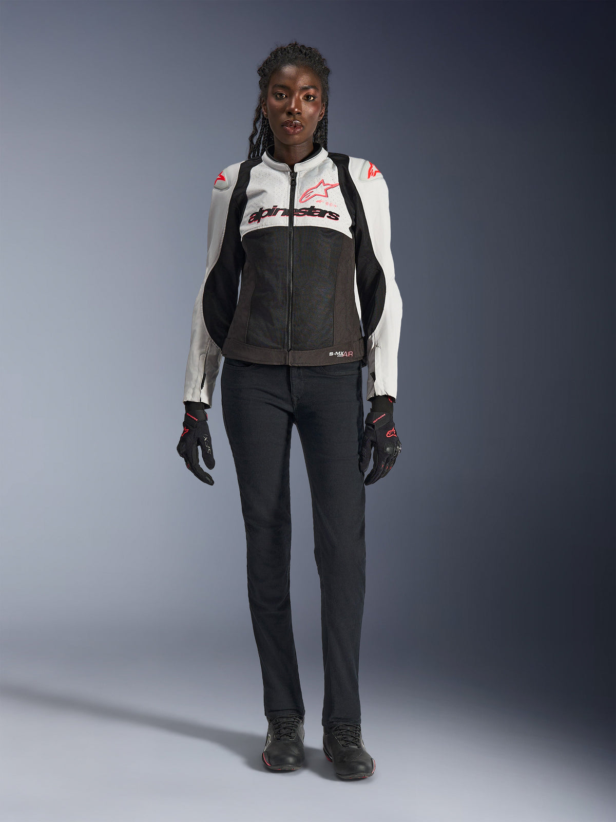 Alpinestars Stella SMX Air Jakke, Ice Gray Black og Coral Fluo, båret af en kvindelig model med sorte motorcykelbukser og handsker, med mesh-chassis og beskyttende skuldersliders, sportsmotorcykeludstyr til kvinder
