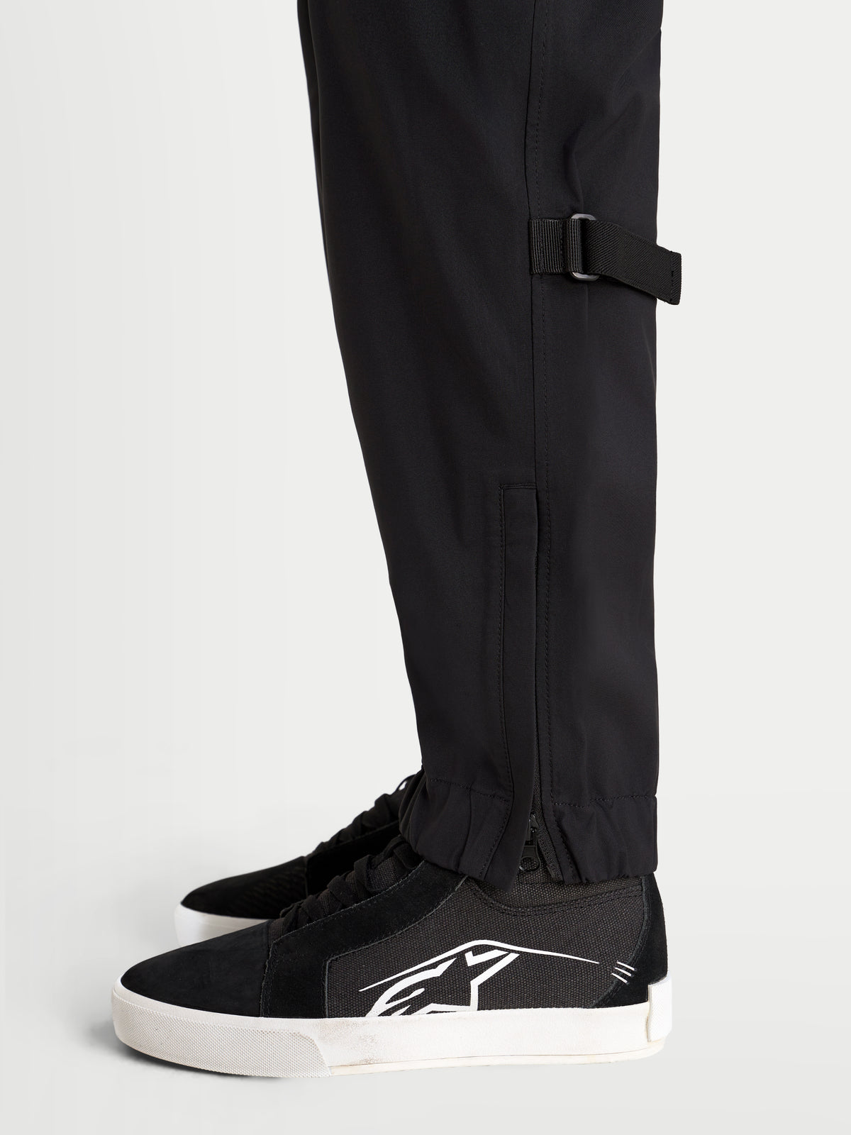 Alpinestars Juggernaut V2 Drystar® Pants, men's waterproof urban motorcycle pants in black, close-up side view showing lower leg adjustment and elasticated hem with zippered opening worn by a model