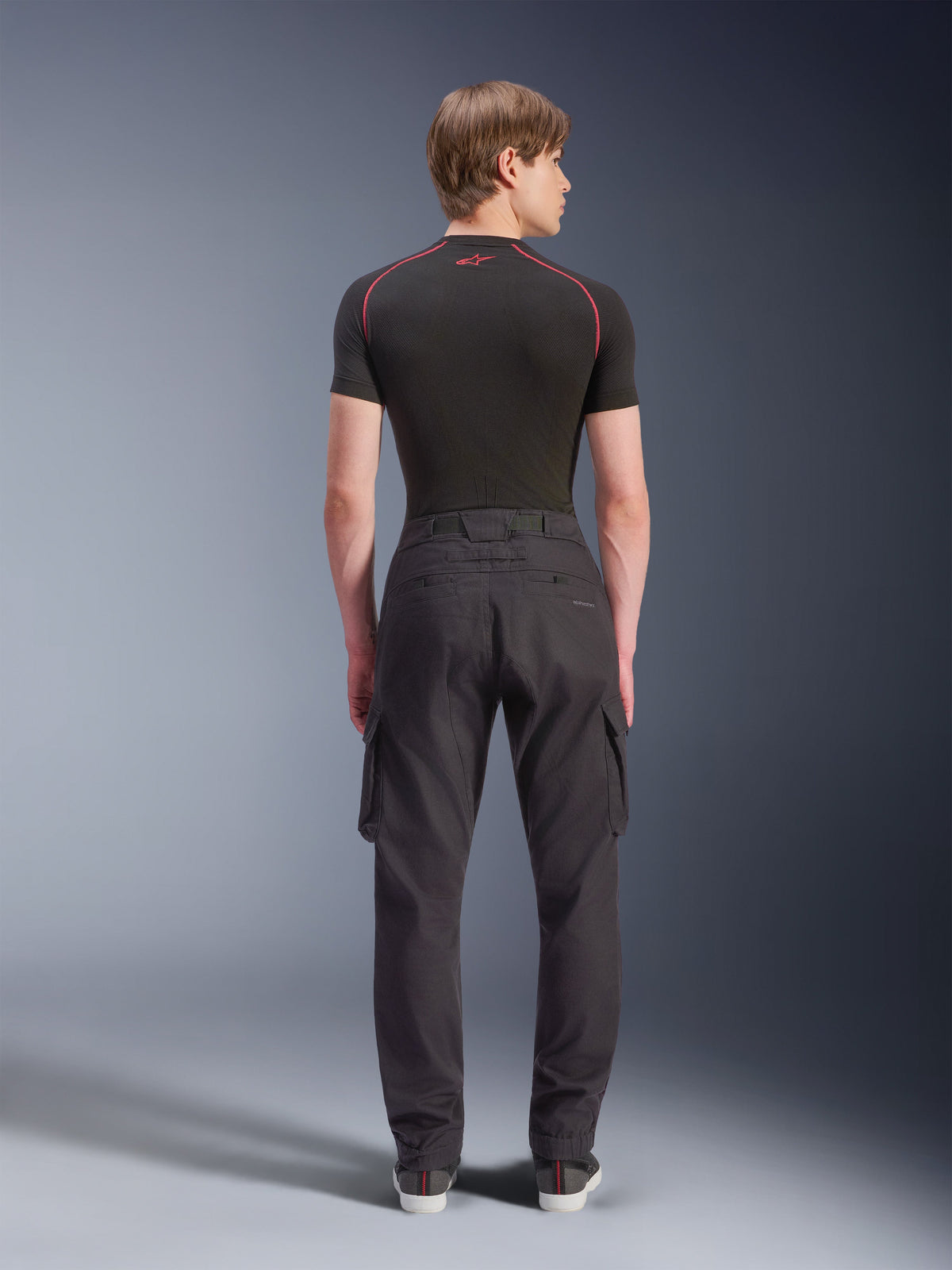 Alpinestars Flex-AST Cargo Pants - Short, sorte urbane motorcykelbukser set bagfra, med cargolommer på siderne og elastiske sømme, båret med et sort kortærmet basislag med røde kontrastsyninger