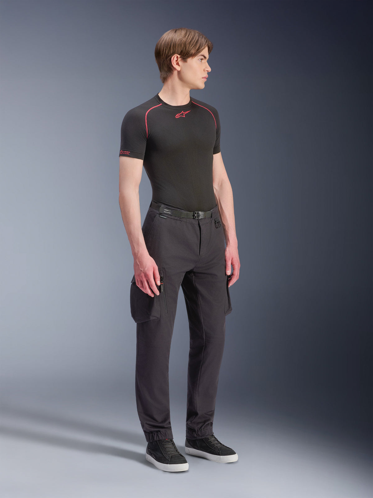 Mandlig model iført Alpinestars Flex-AST Cargo-bukser – Short i sort, urbane motorcykel-cargobukser med sidelommer og tilspidsede ben, stylet med et sort baselayer og sneakers, urbant køreudstyr.